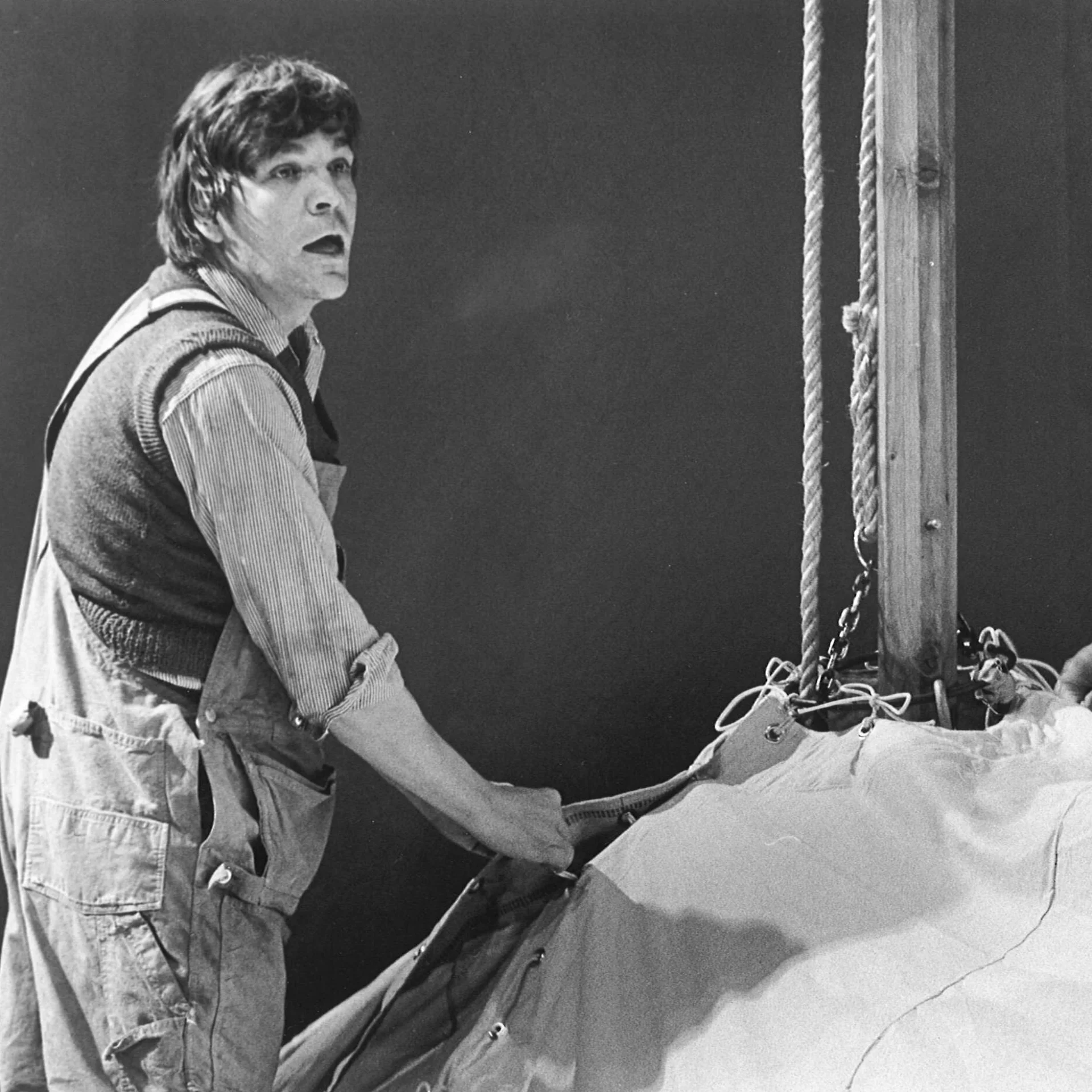 A man wearing overalls is scene fixing a harness on a wooden pole.