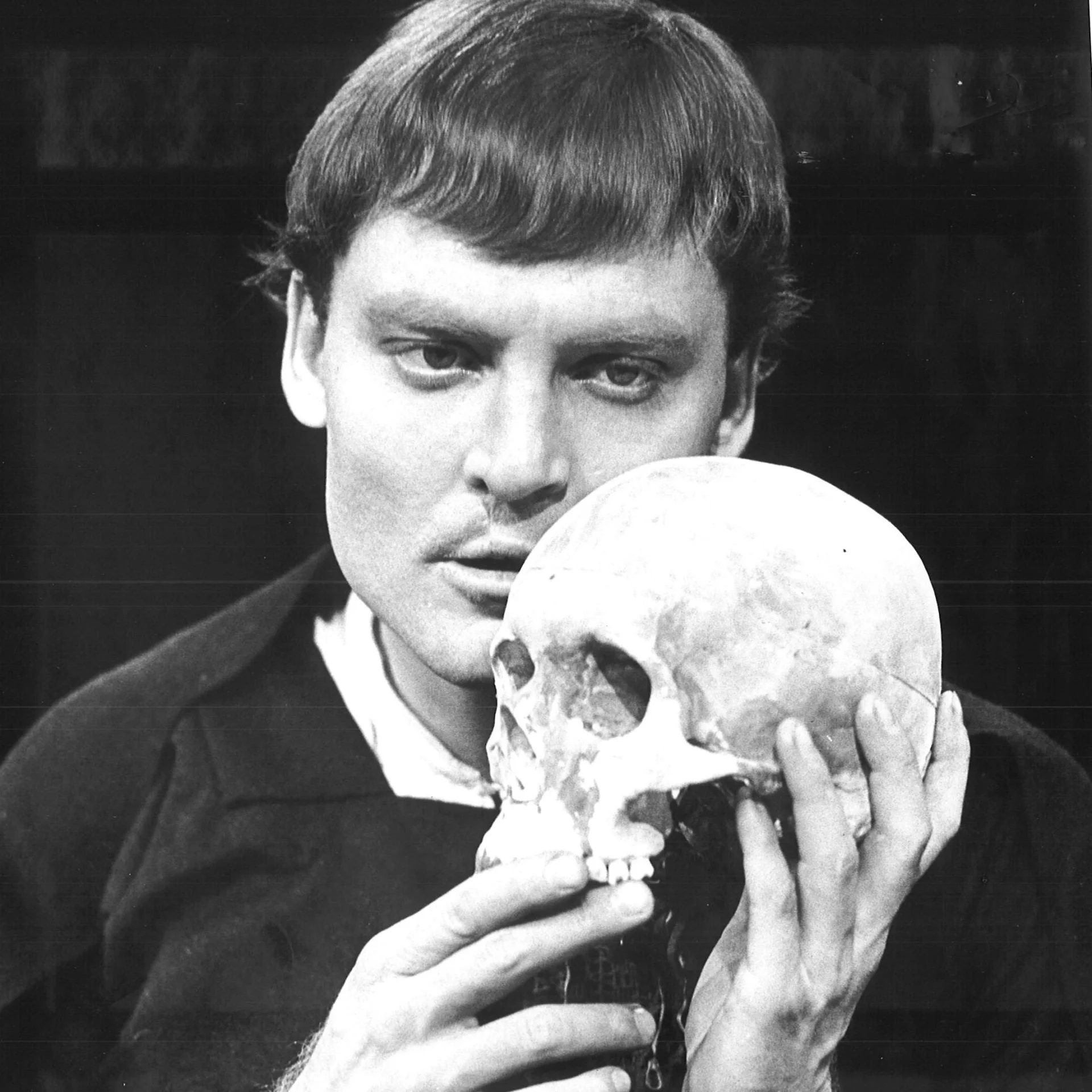 A man is seen holding a skull and looking at it.