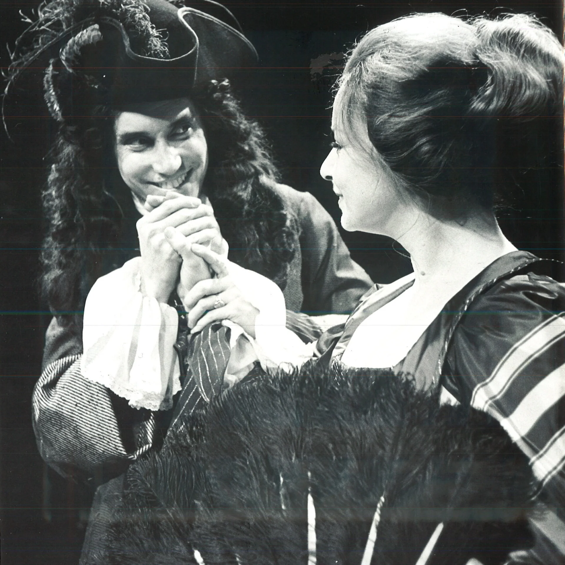 A man is seen wearing a pirate hat and talking to a woman who's holding a feathered fan.