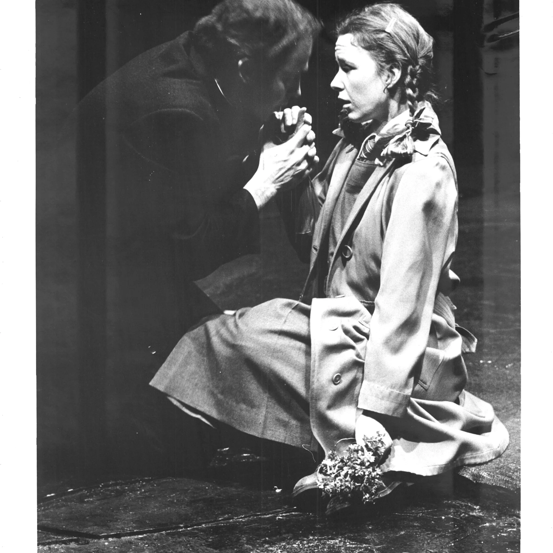 A young girl with braids is sitting down with flowers in one hand while the other is holding a mans hand.