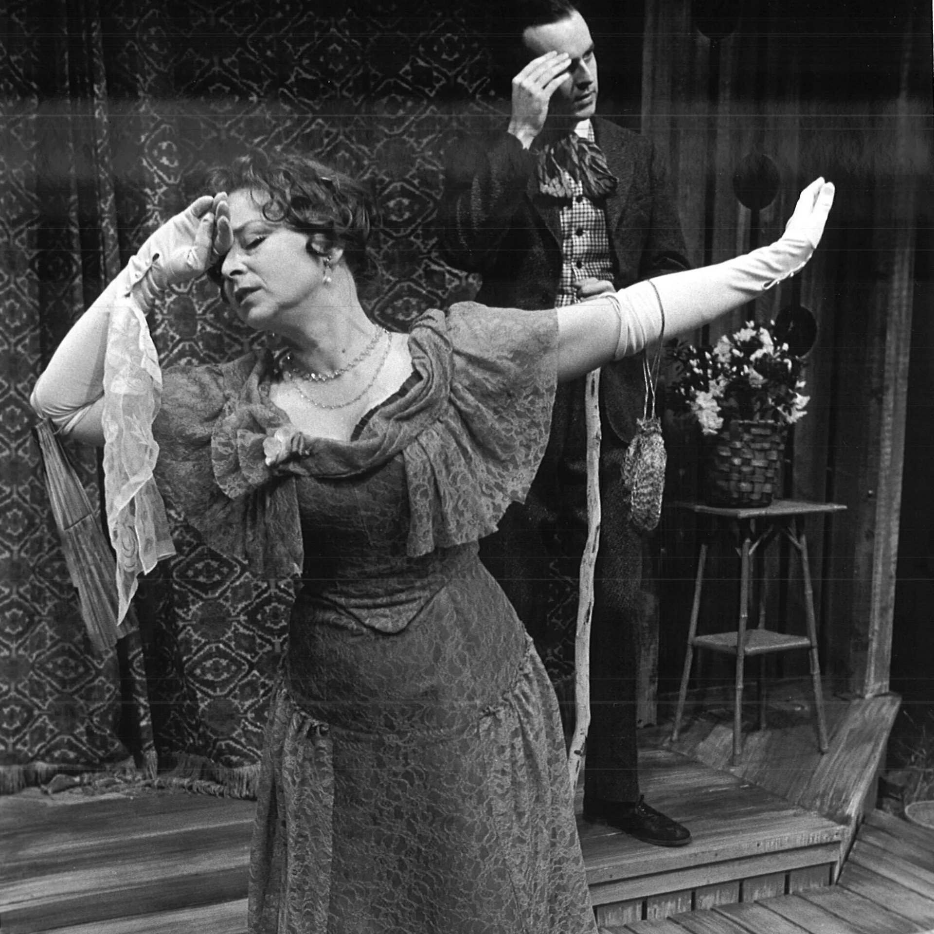 a woman is seen putting a hand to her forehead and the other hand to the back of her while the man in the background is pinching his temple