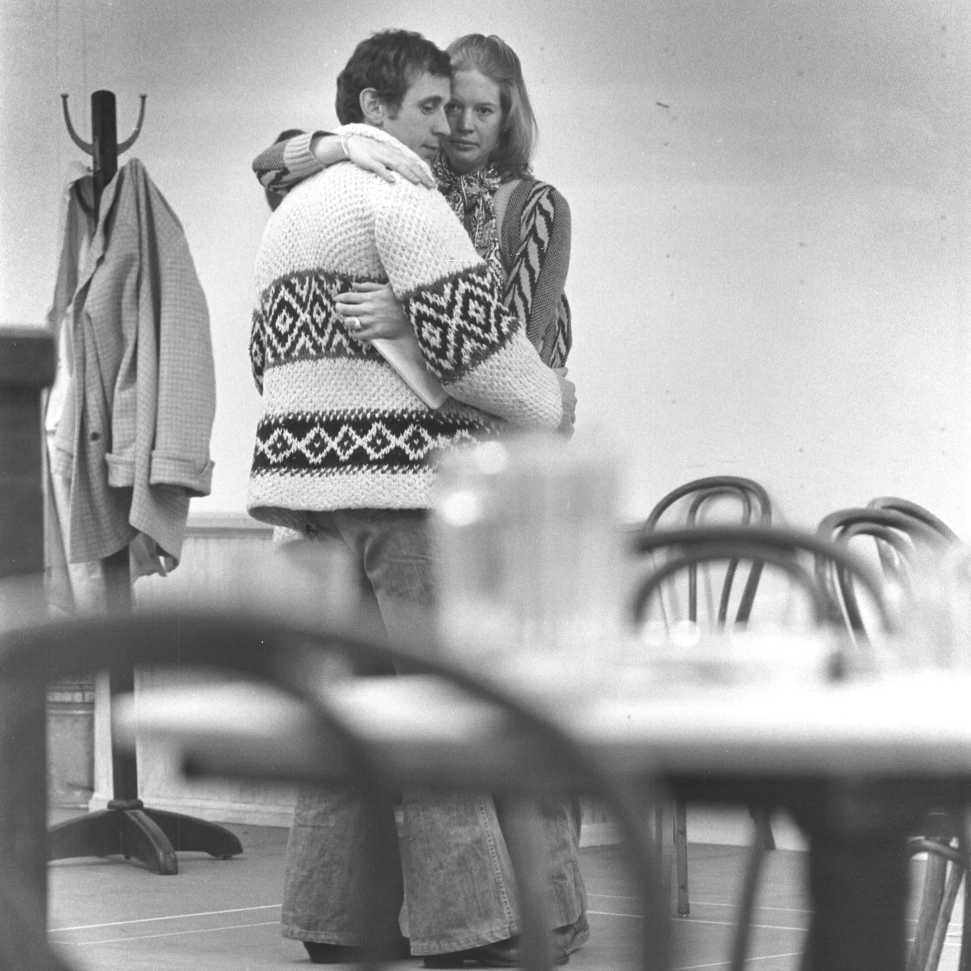 A woman and man are seen behind a table holding each other.