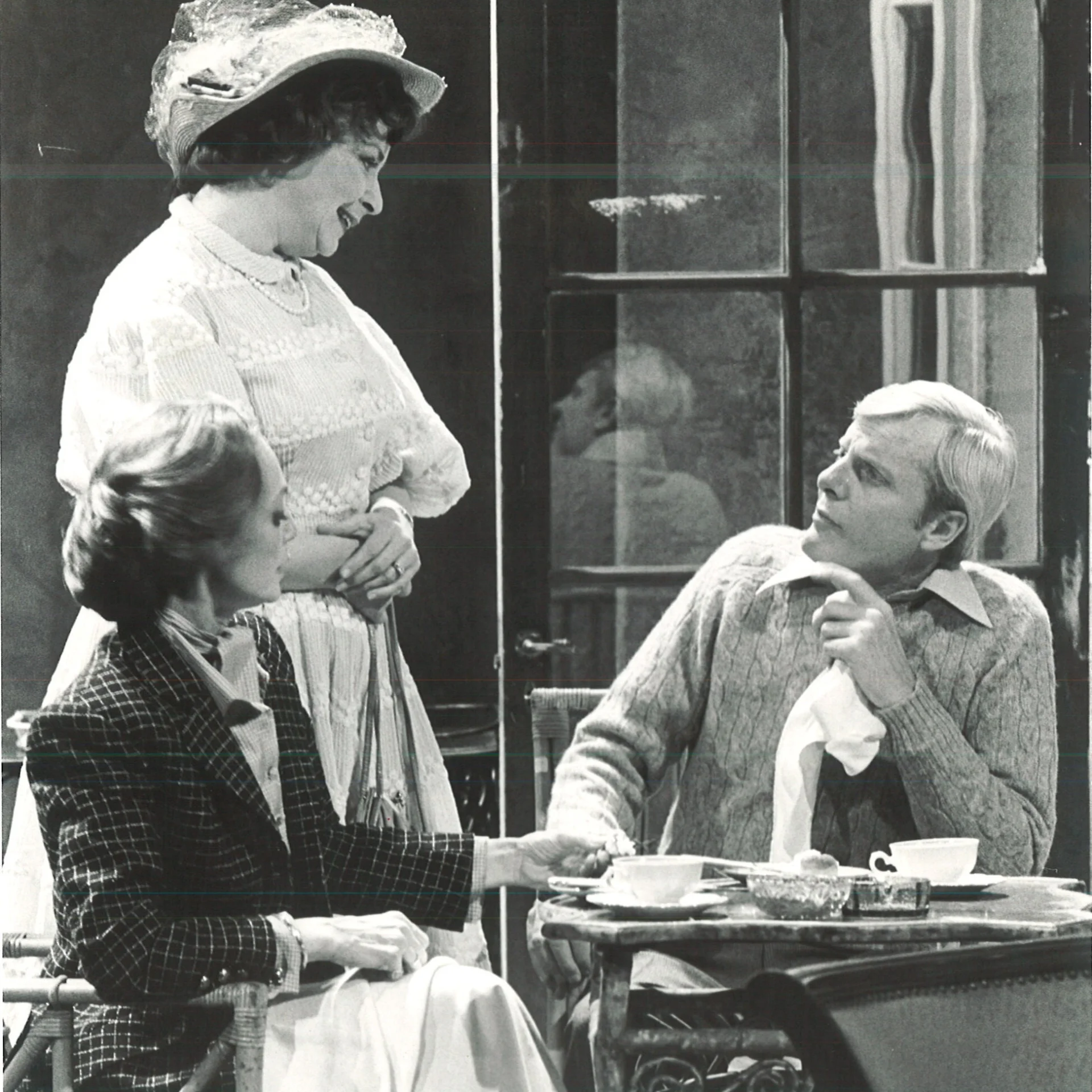 A Man and woman are sitting at a table listening to another woman who is standing over them.