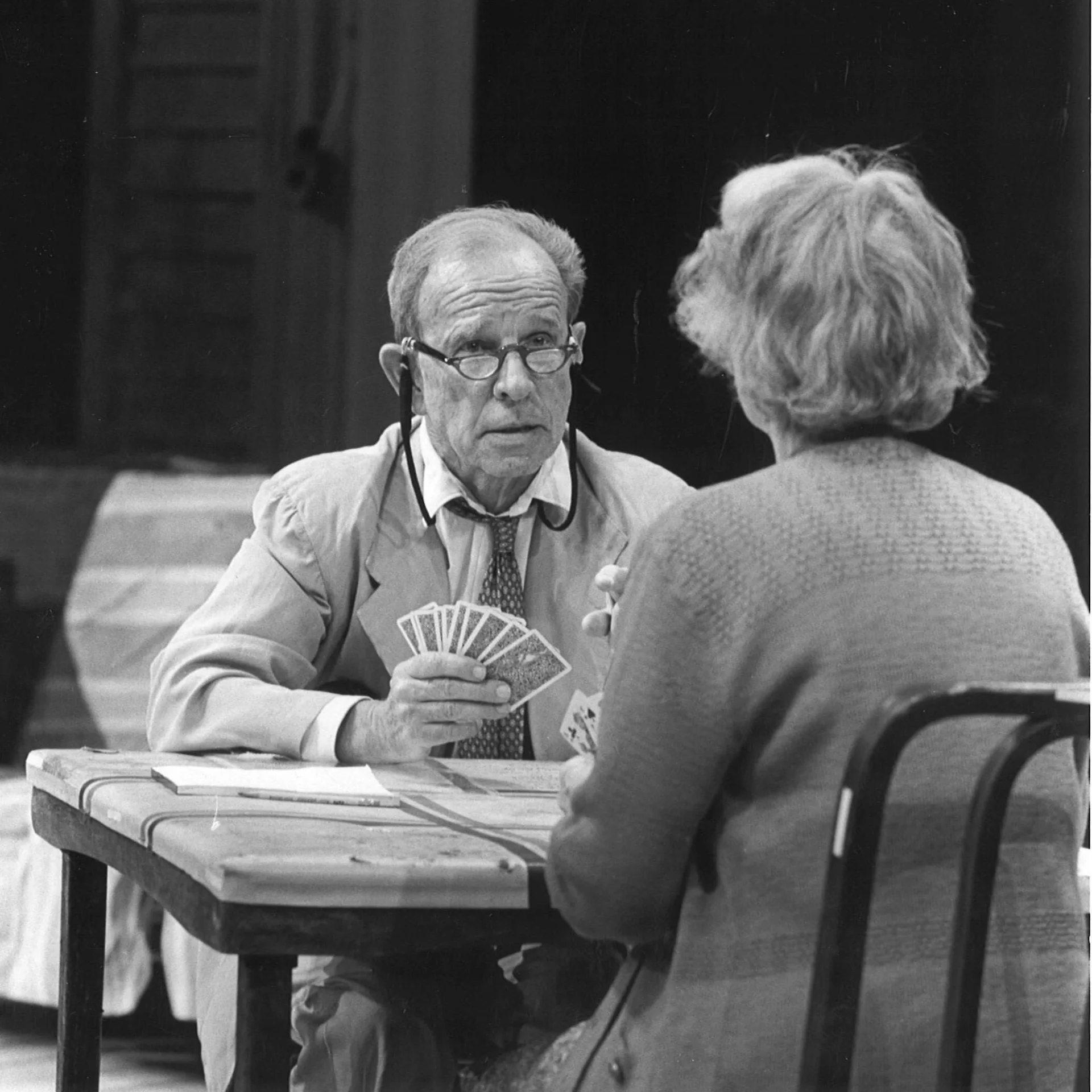 A man and woman are seen sitting across from each other at a table and the man is holding a deck of cards