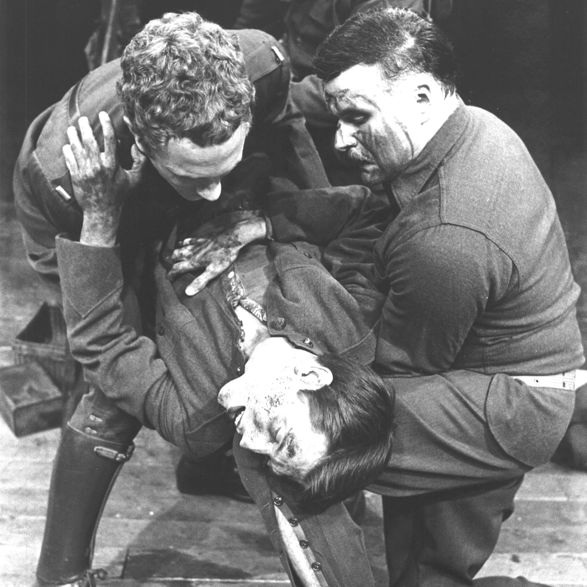 Two men wearing army suits  are seen holding up another man who appears to be unconscious and or dead.