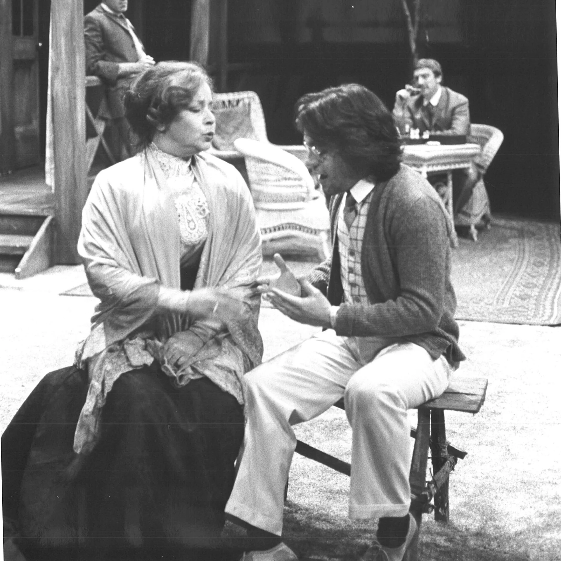 A man and woman are seen sitting together and talking, the woman has an annoyed face and is reaching for the mans hand.