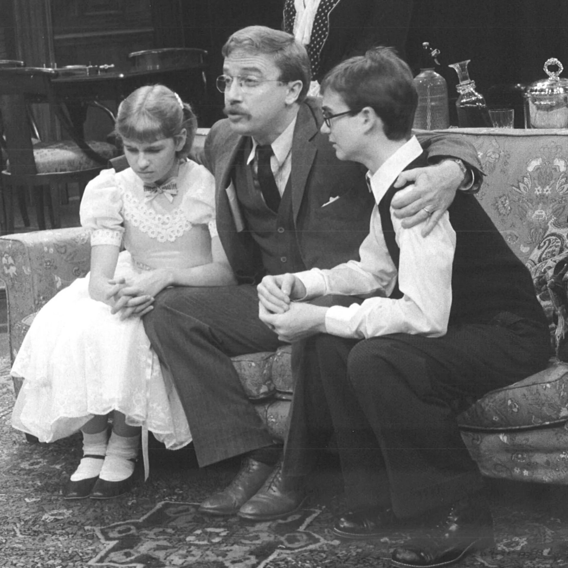 A Man is sitting on the couch with a young boy and girl and has his arms wrapped around both of them.