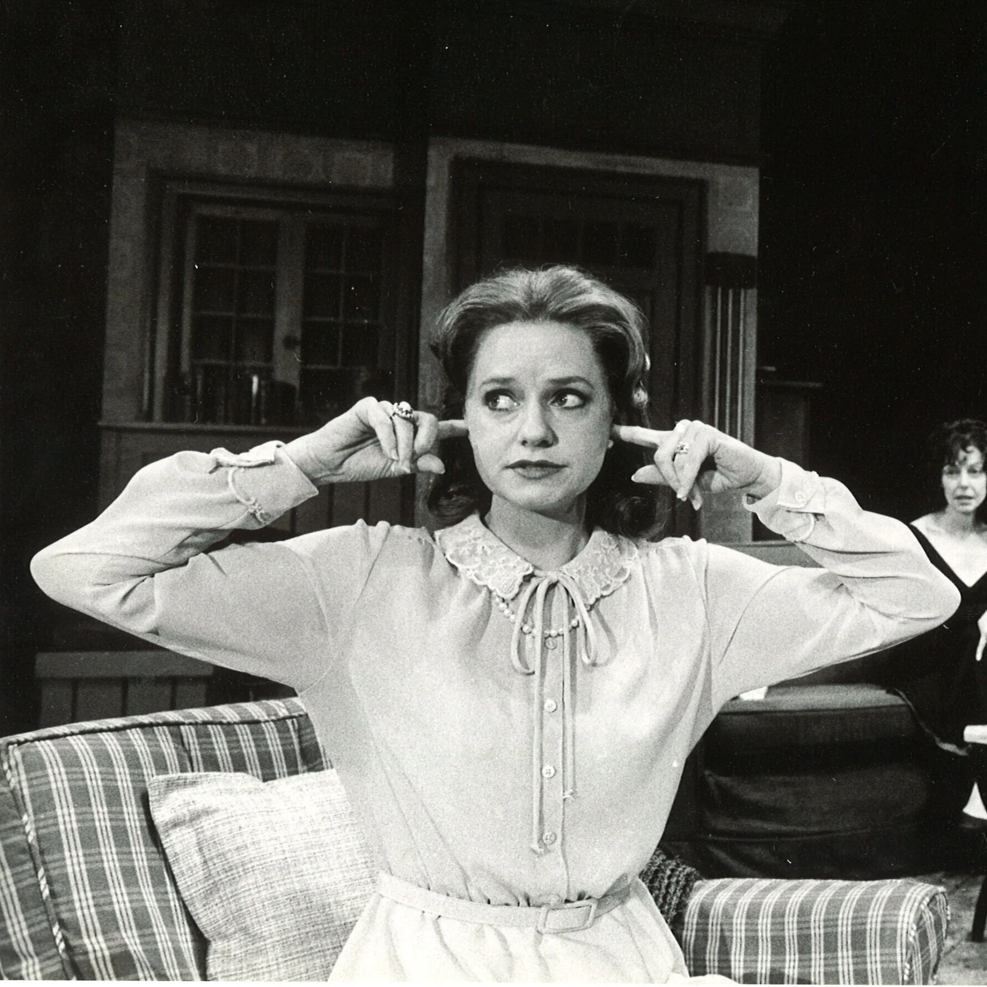 A woman is seen sitting on a couch and plugging her ears while she looks away