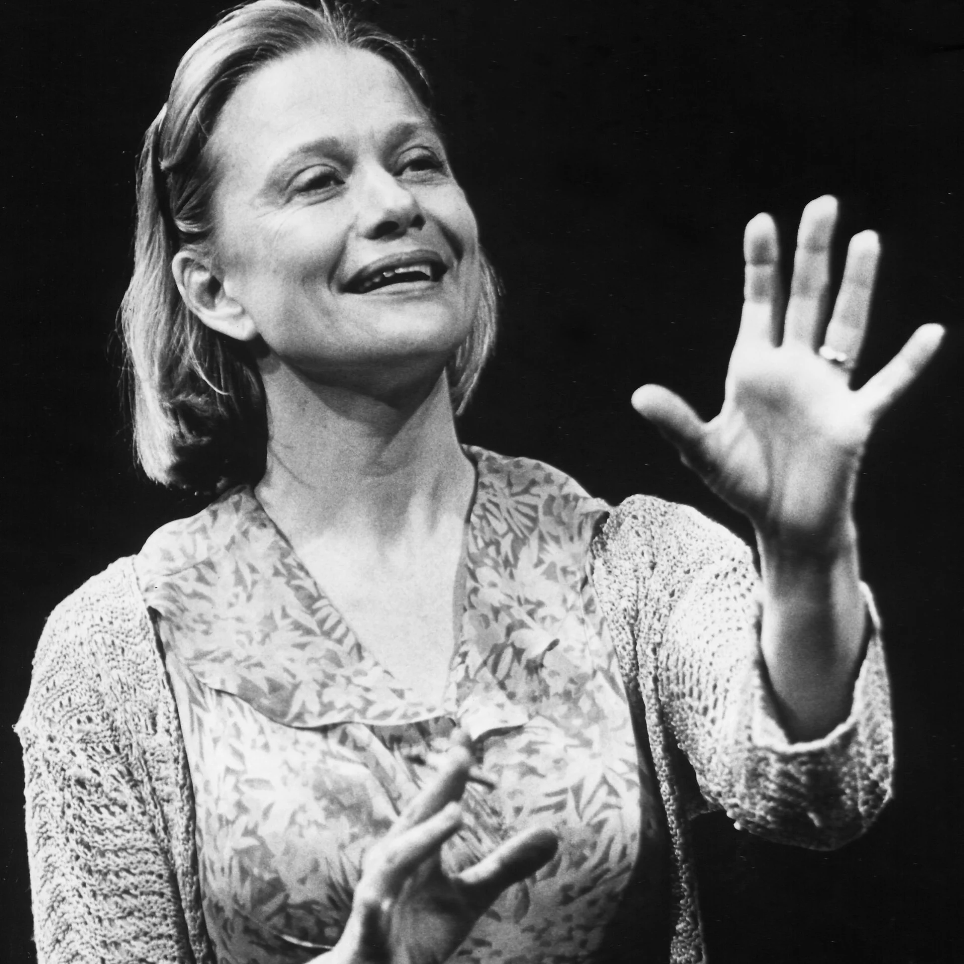 A smiling woman holds up her hands while speaking