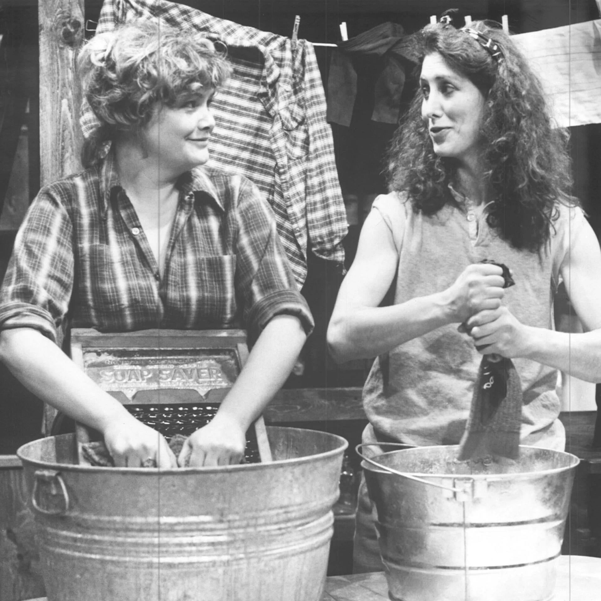 Two woman are washing their clothes together in washing pans.