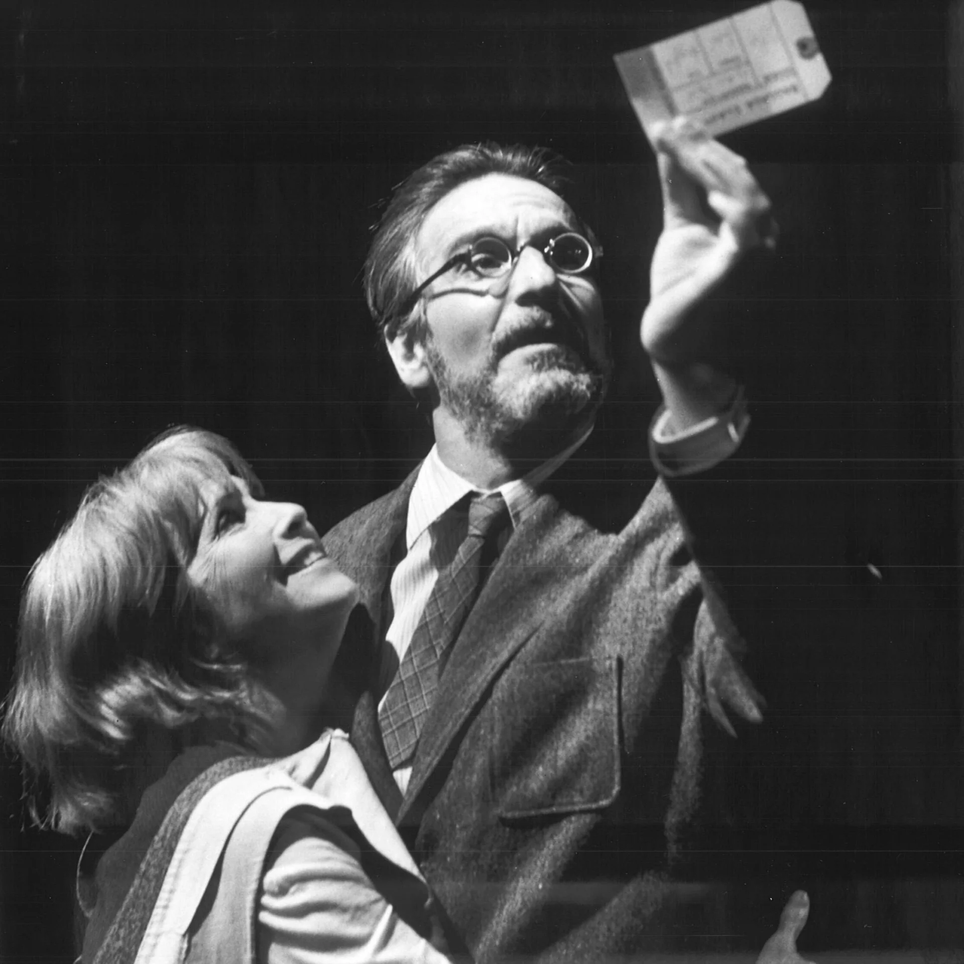 A woman is hugging a man while he is holding up a clothing tag.