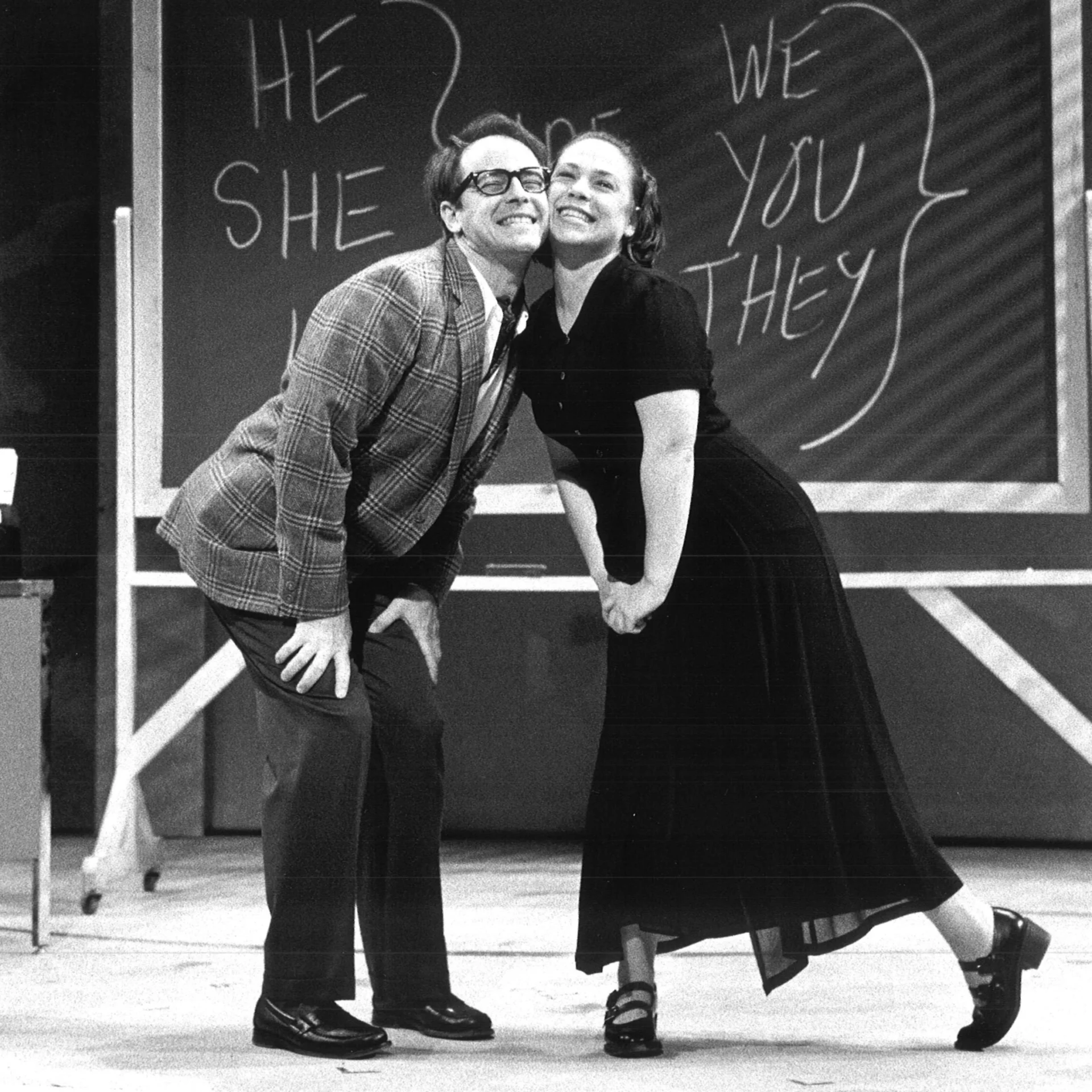 A man and woman pose cheek-to-cheek in front of a chalkboard with pronouns