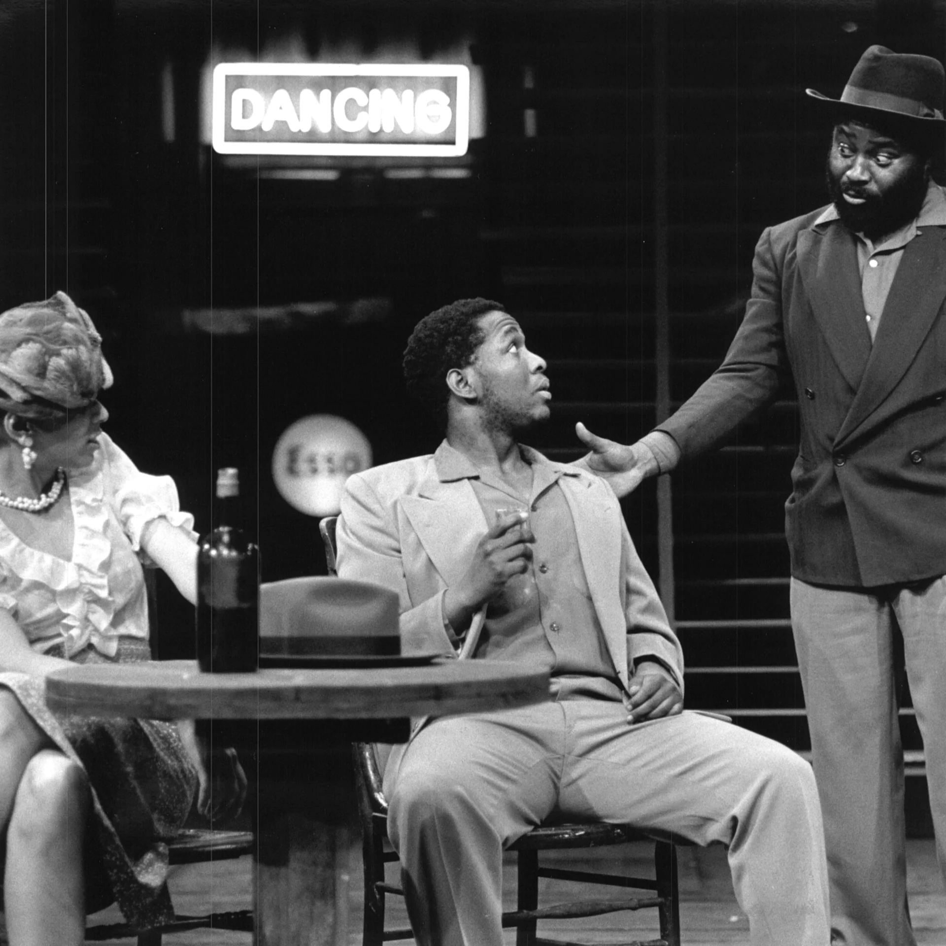 A man and woman are sitting at a table together while another man is standing beside them talking to them.