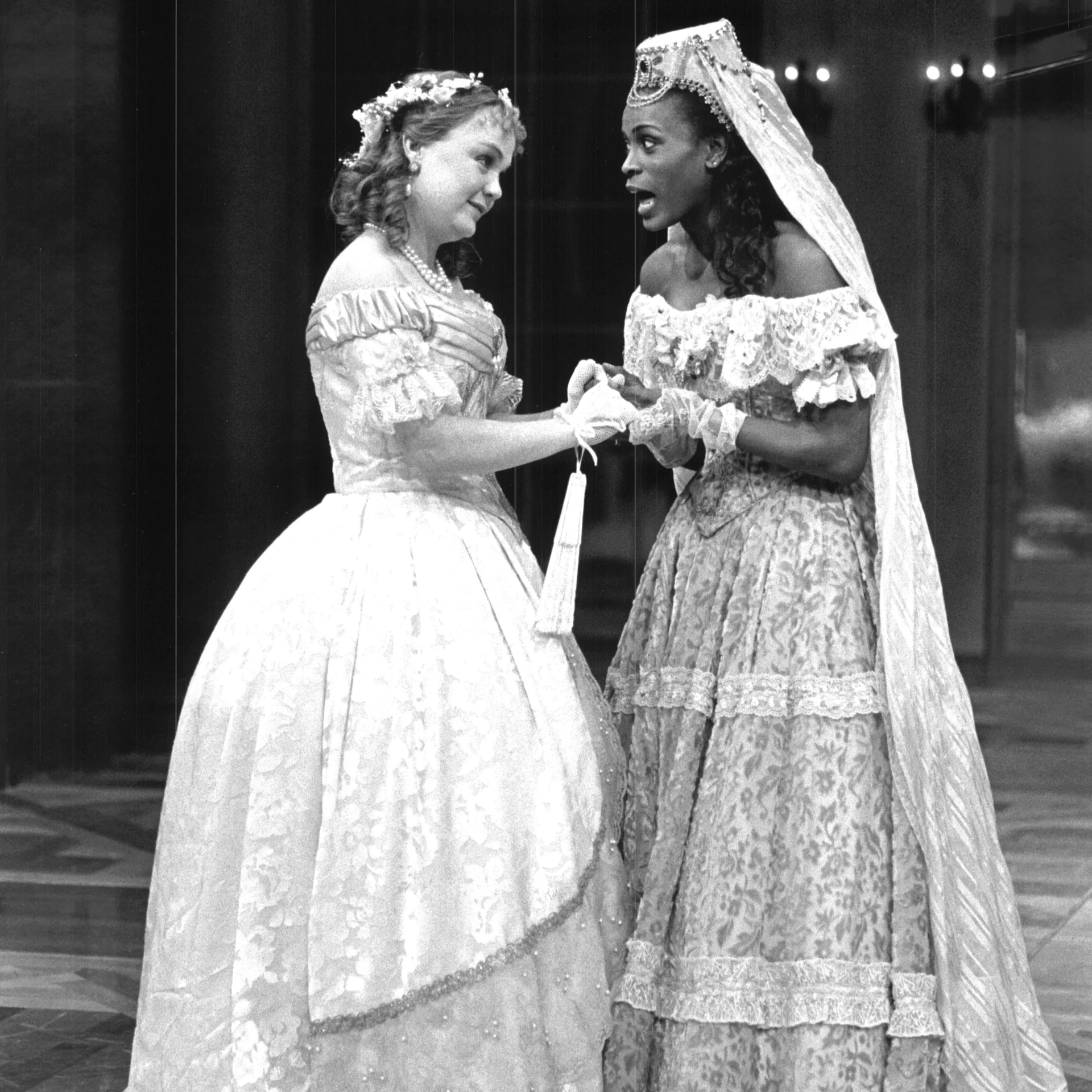 Two women wearing ballgowns are standing together having a conversation.