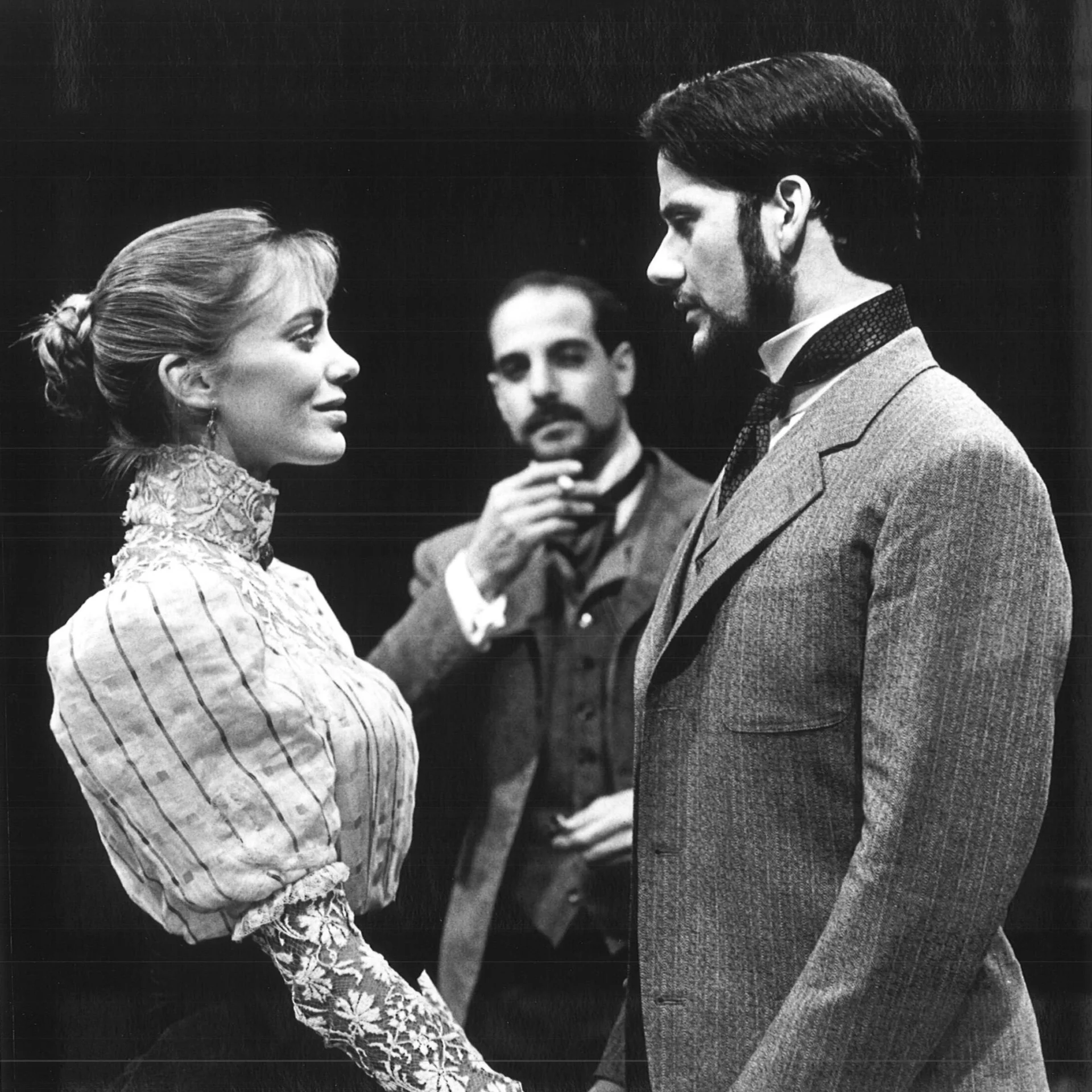 A man and woman ae standing across from each other holding hands while another man is watching in the background.