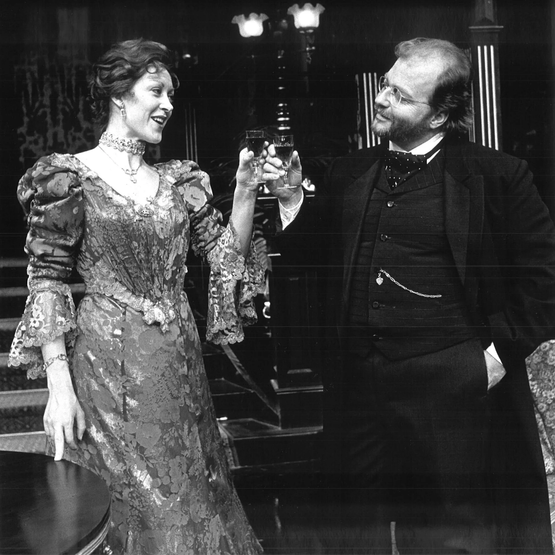 A woman in a Victorian style dress is toasting a glass with a man in a suit.