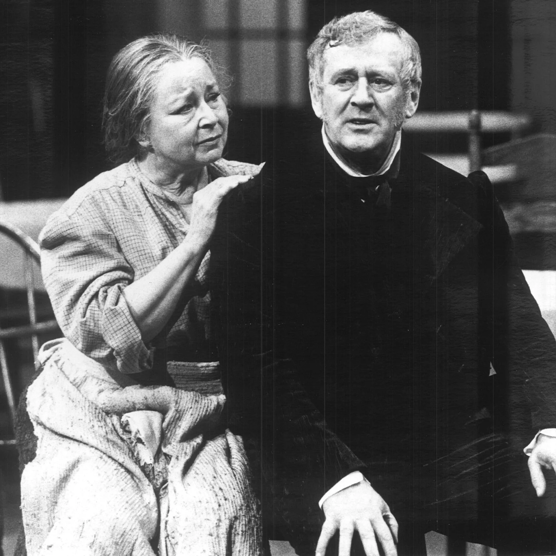 A woman is sitting beside a man putting her hand on his shoulder.