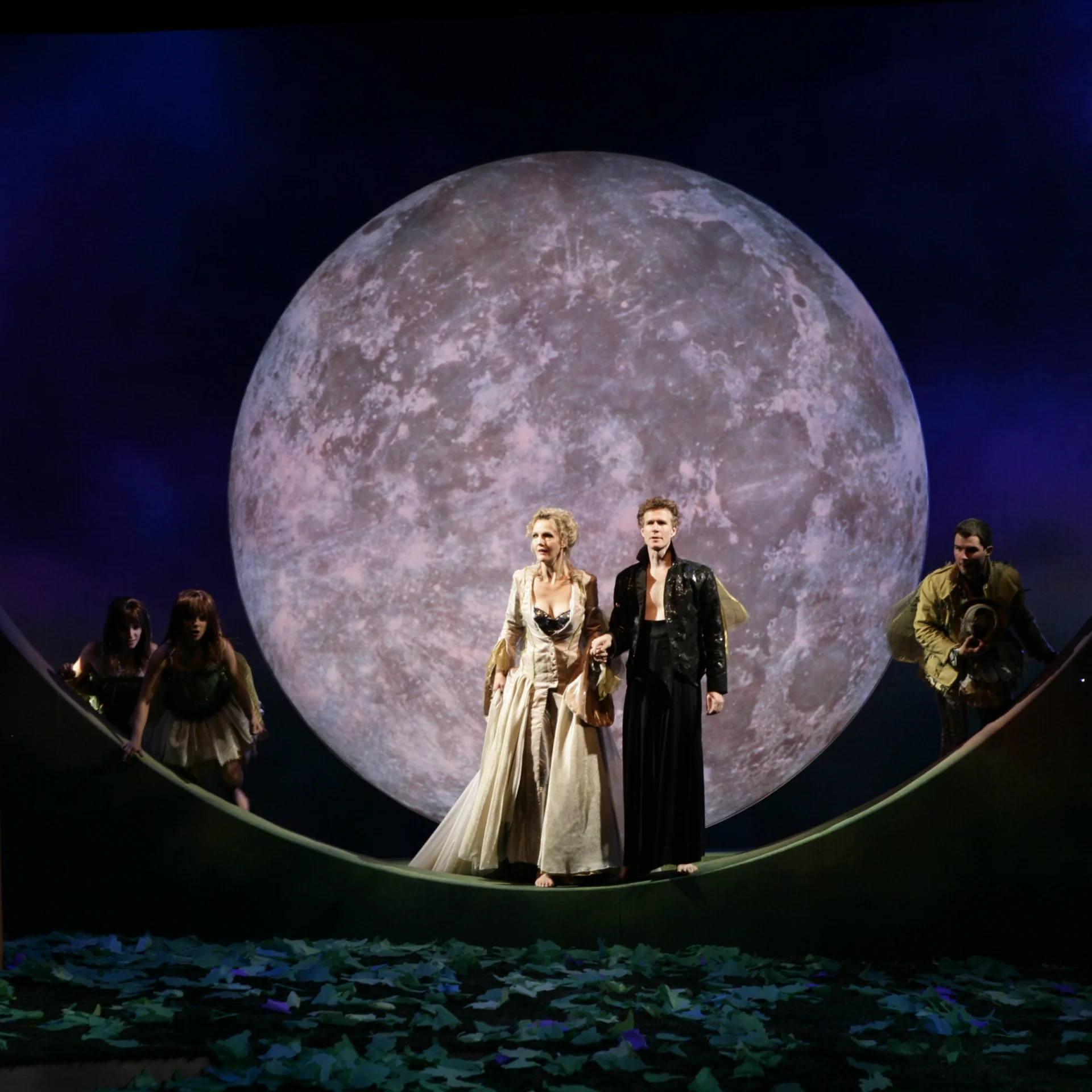 A man and woman stand together with the moon as their backdrop