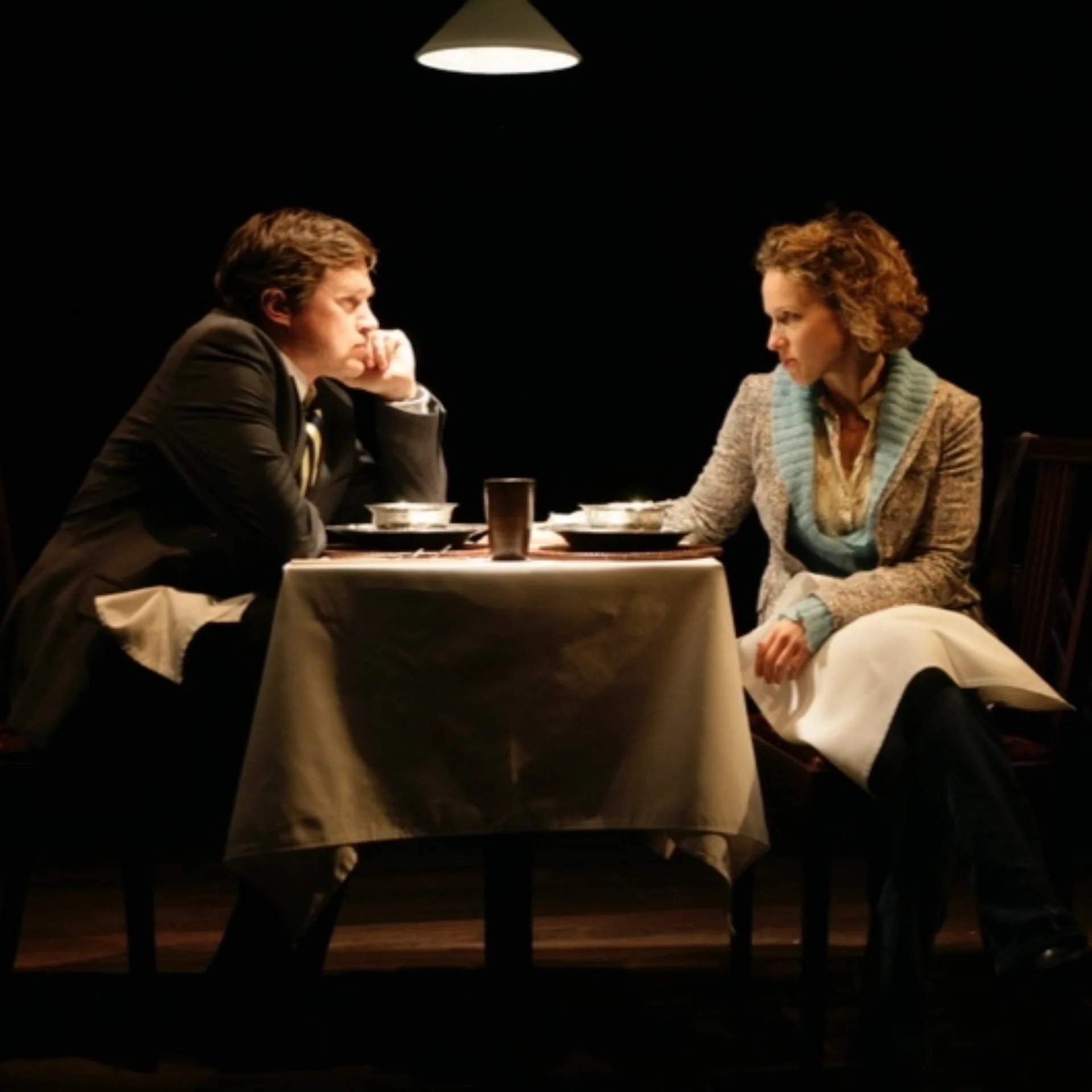 A man and woman sit at a dimly-lit table looking at each other