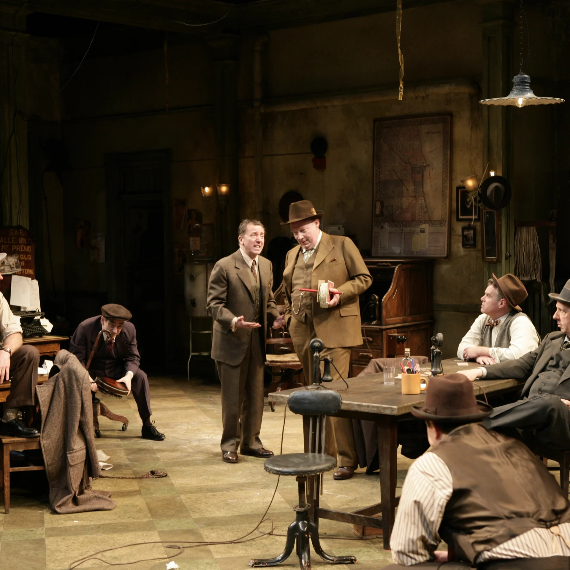 A group of men gather in a newsroom sitting down; two men in the center are standing