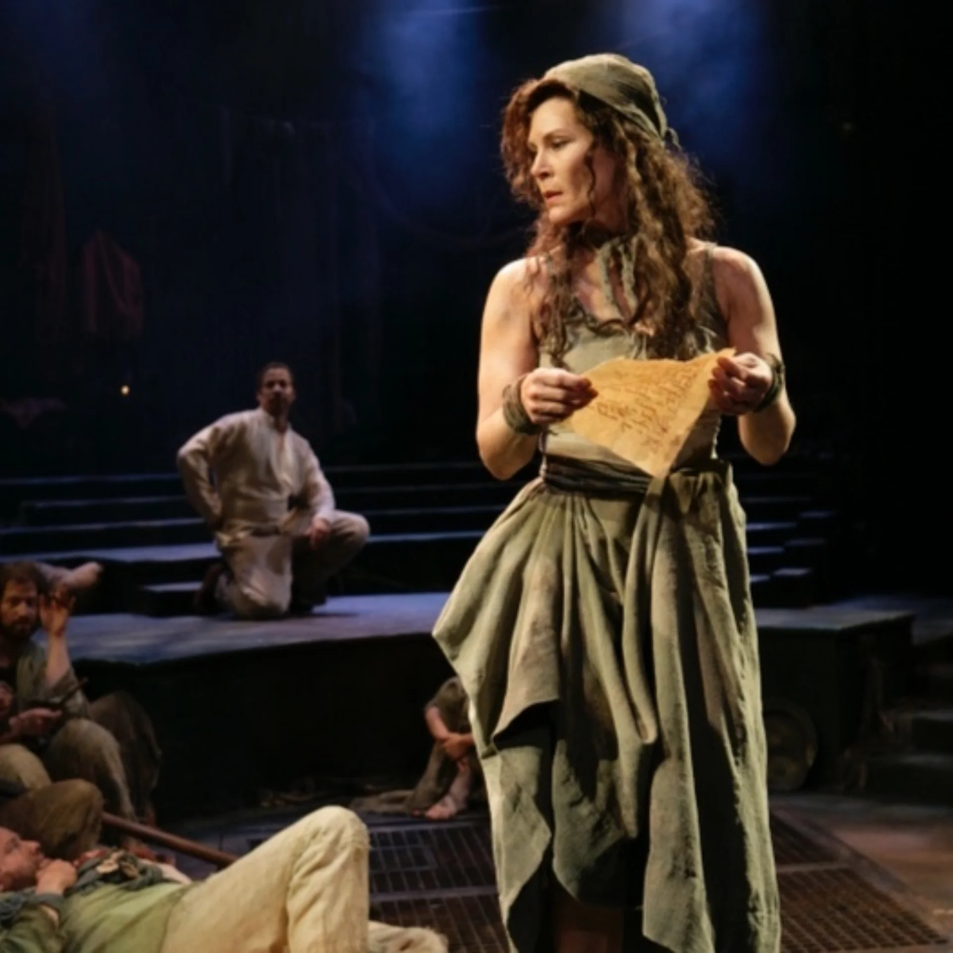 A woman dressed in rags holds a ripped parchment and looks off to the side