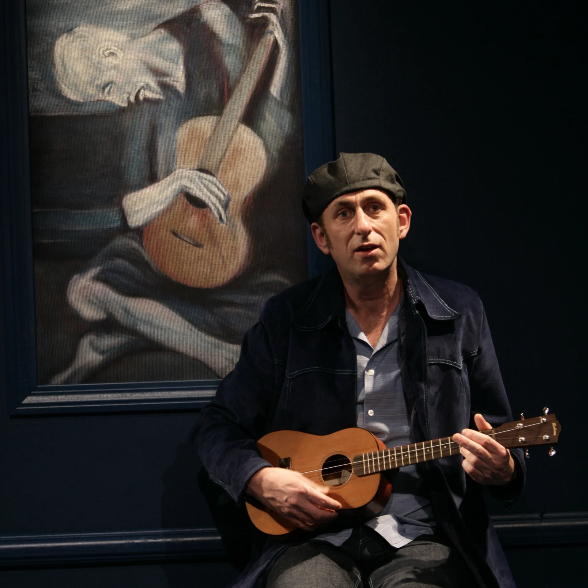 A man sits in front of Picasso's painting, "The Old Guitarist," bearing an uncanny resemblance