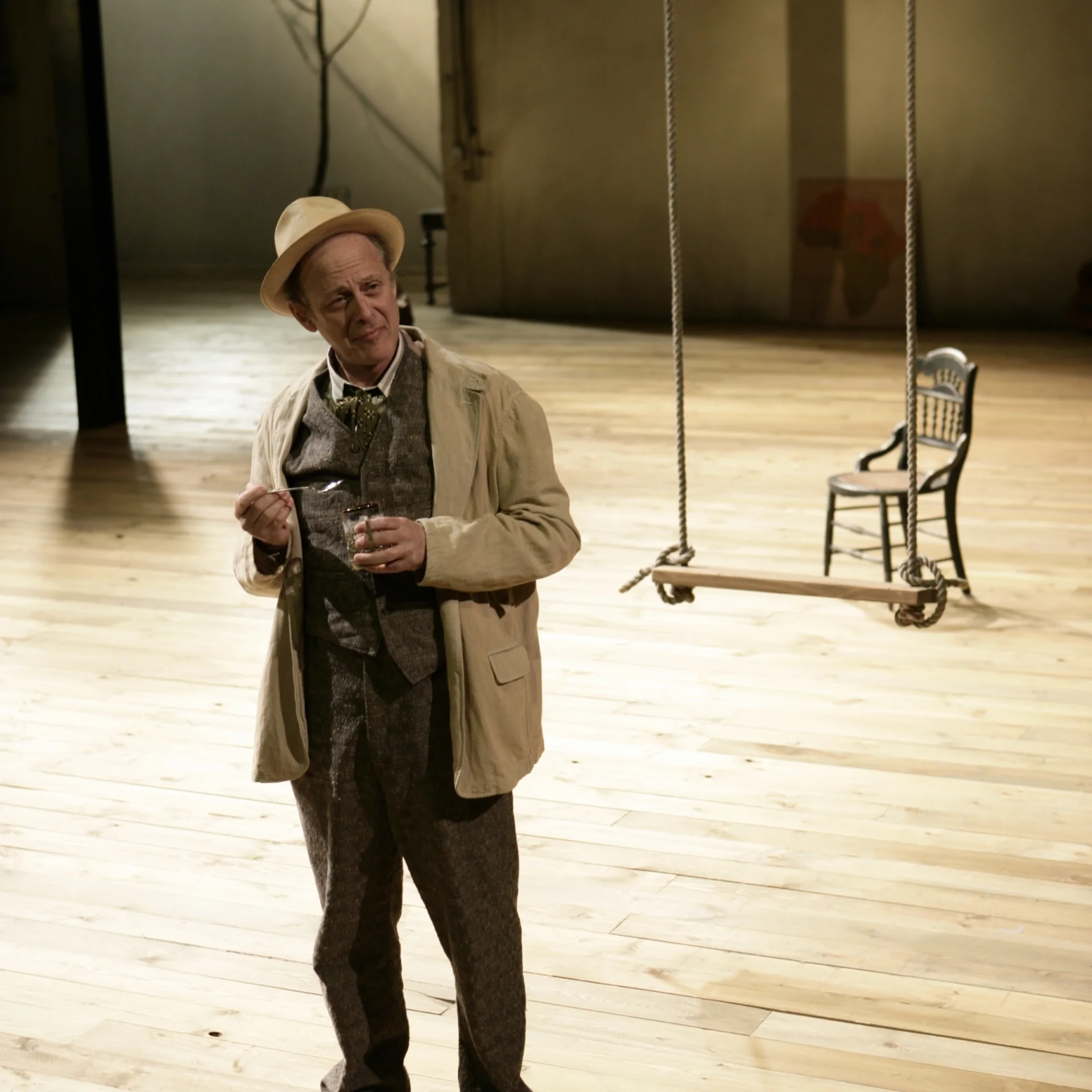 A man holding a cup of tea stands on a wooden stage in front of a swing
