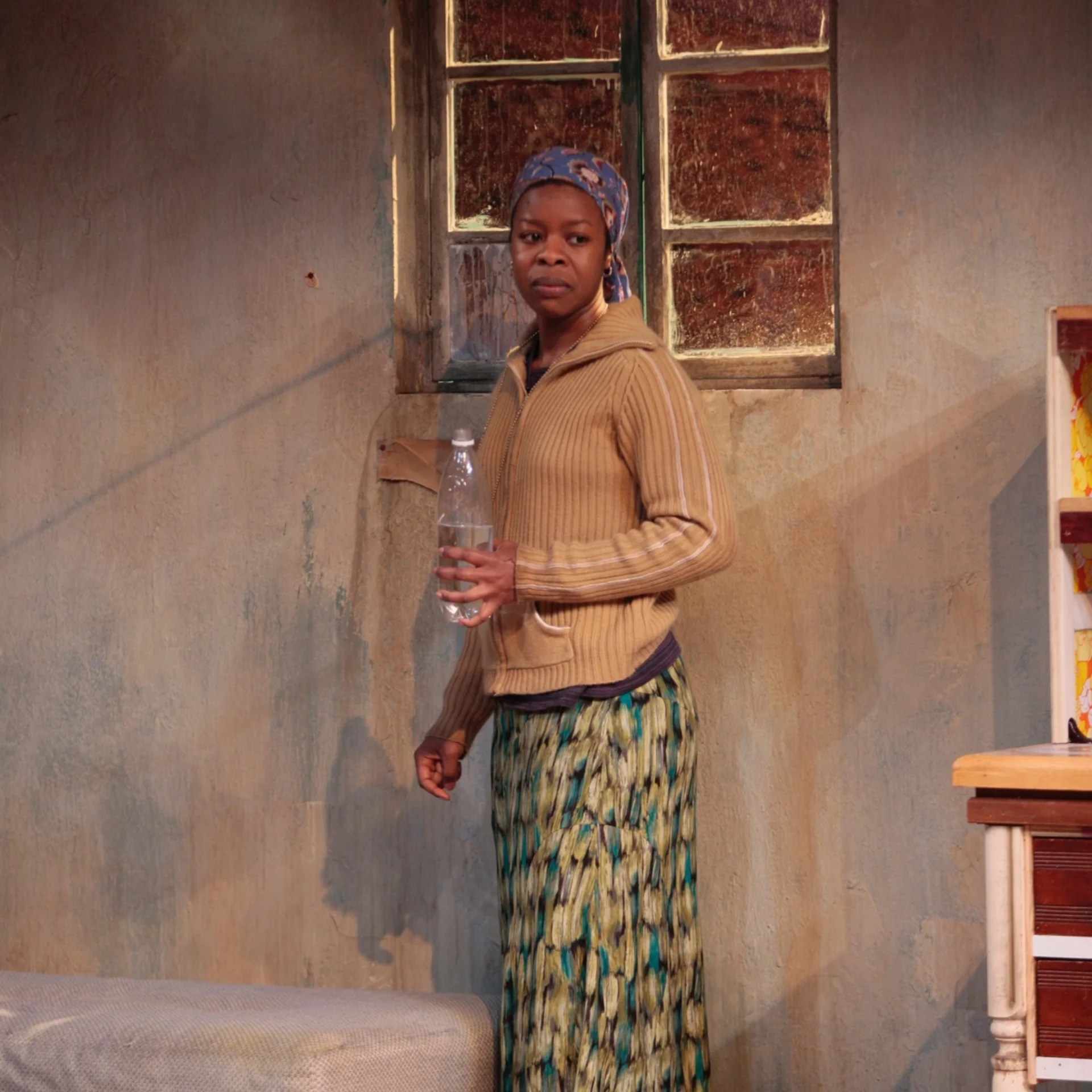 A woman stands in front of a window holding a water bottle