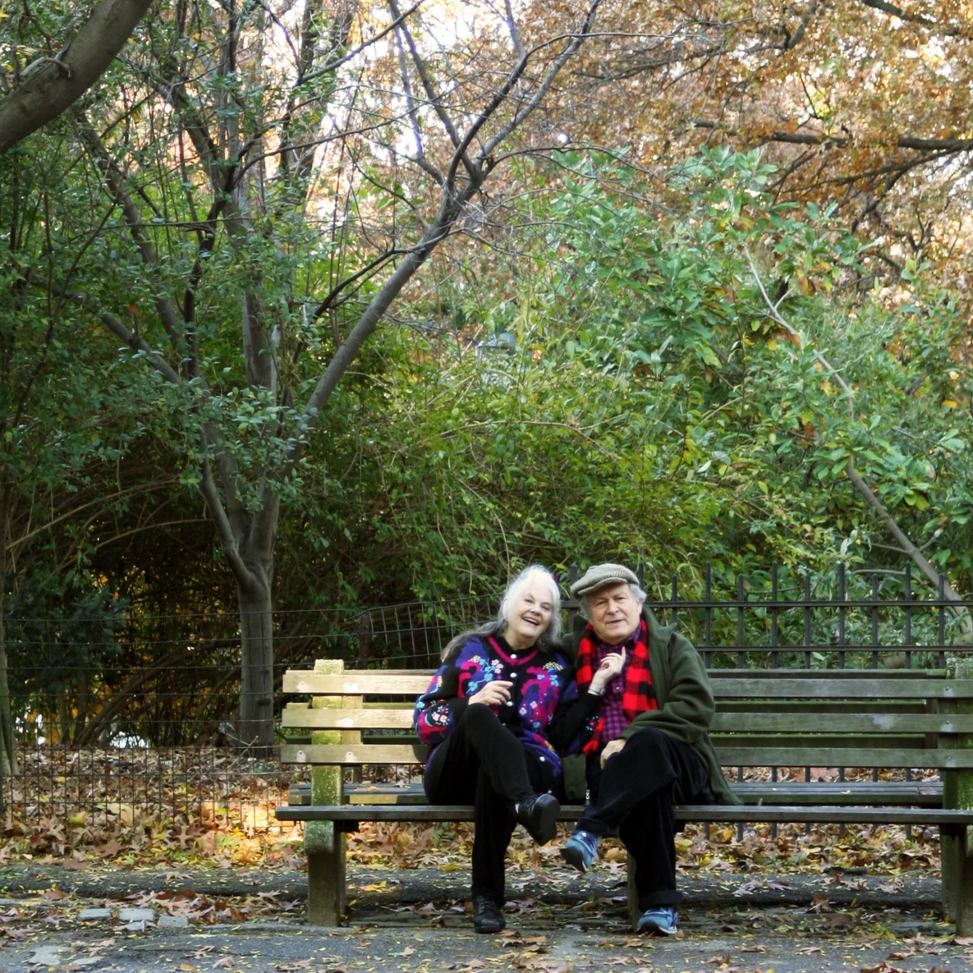 An elderly man and woman sit side-by-side on a bench outdoors