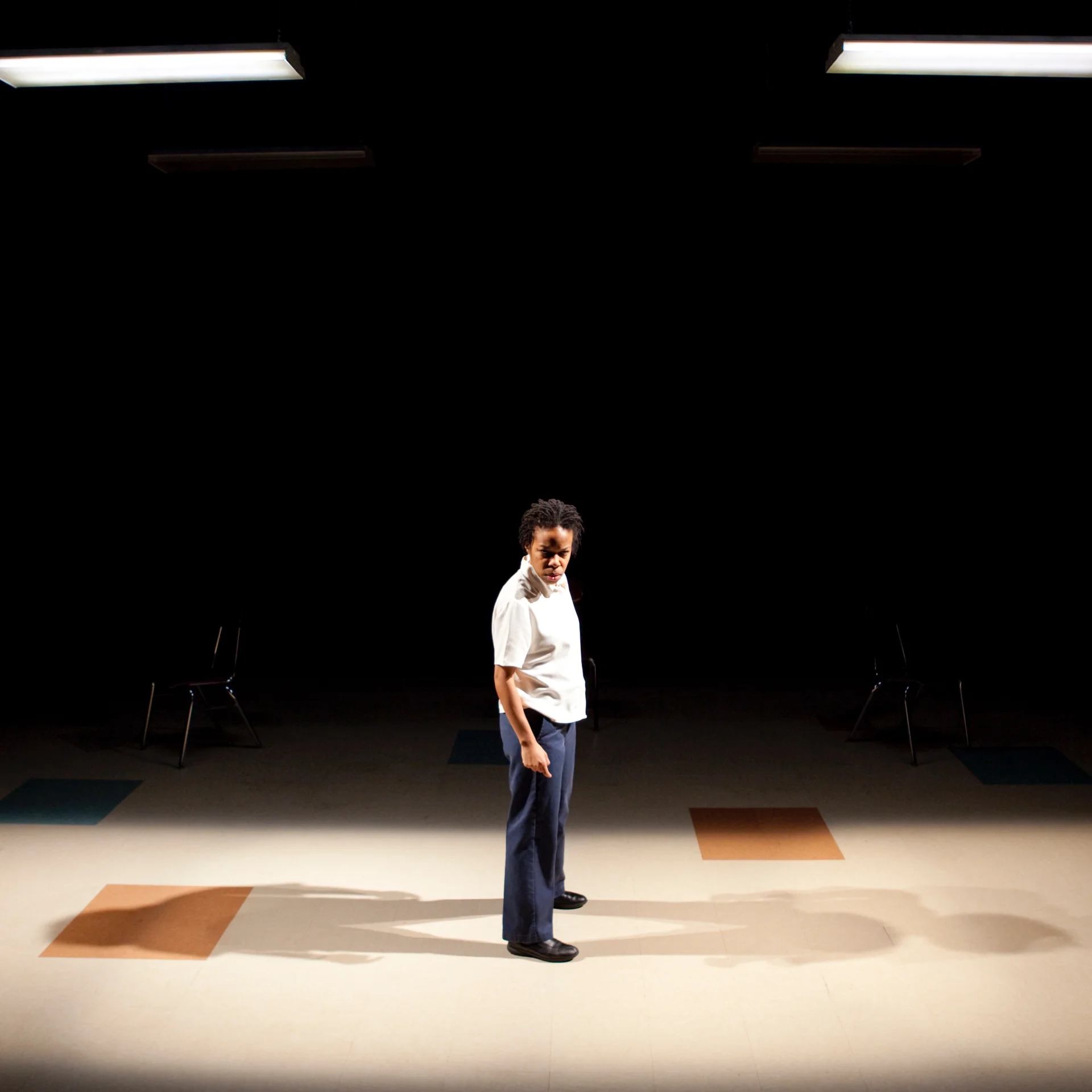 A woman stands on a empty stage on a tiled floor