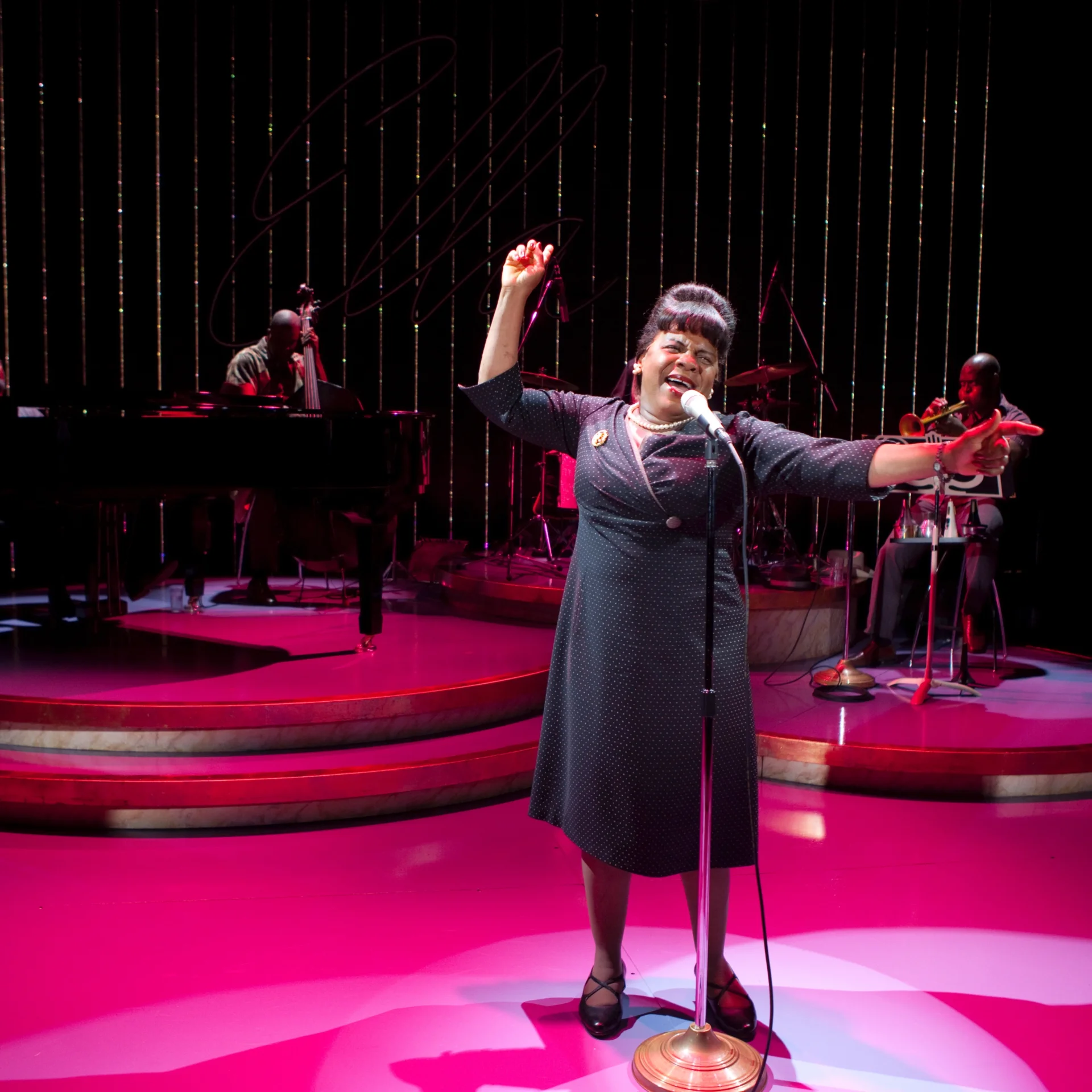 A woman sings into a microphone with a band behind her