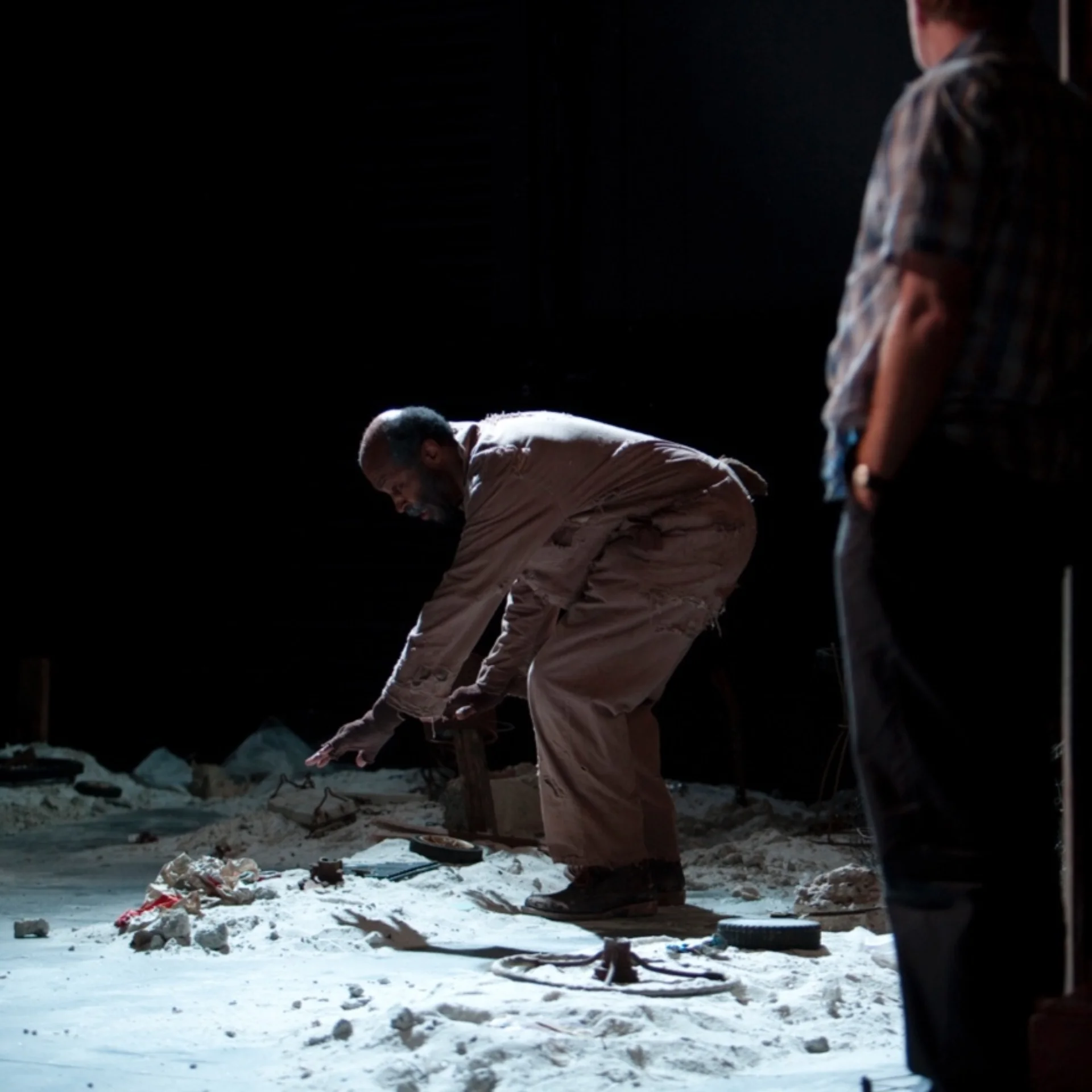 A man bends over rubble while another man looks on in the foreground