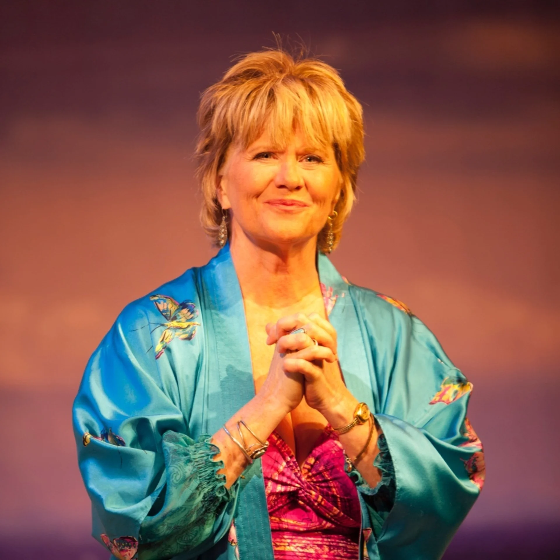 A woman in a blue shiny robe stands with her hands clasped together