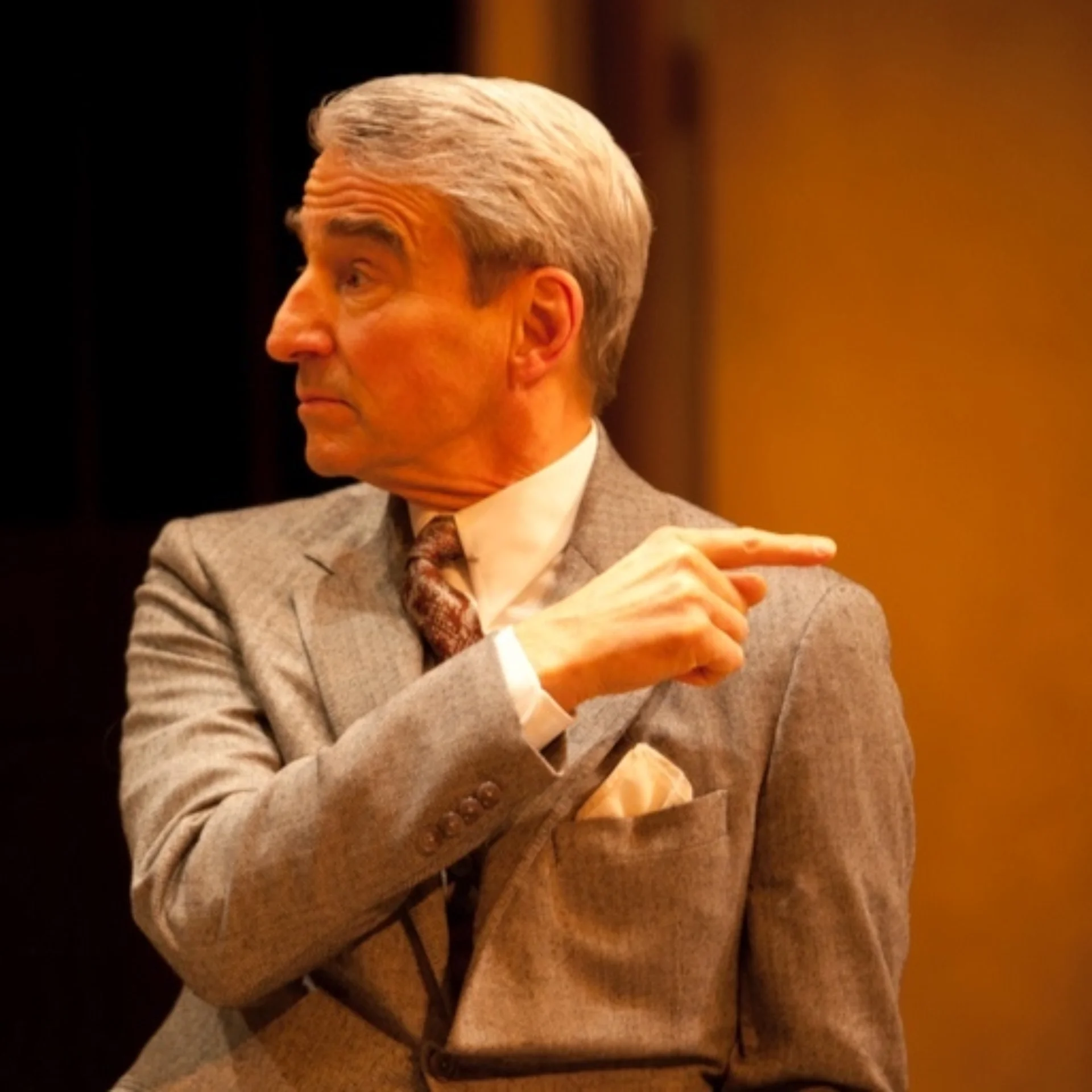 A man in a grey suit looks to his right while pointing to the left