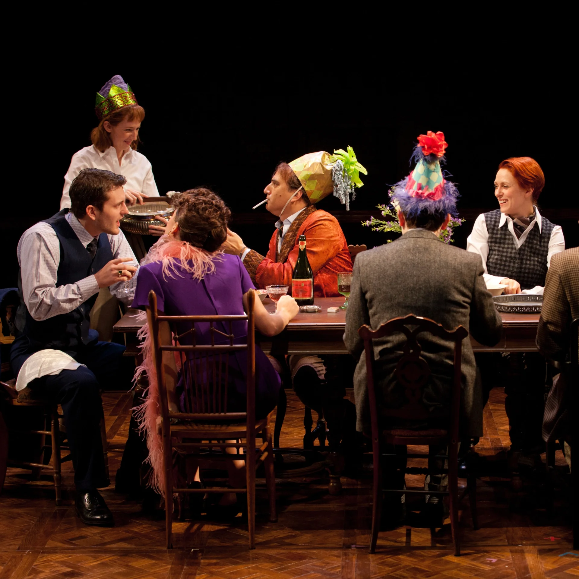 Several people sit at a table donning party hats