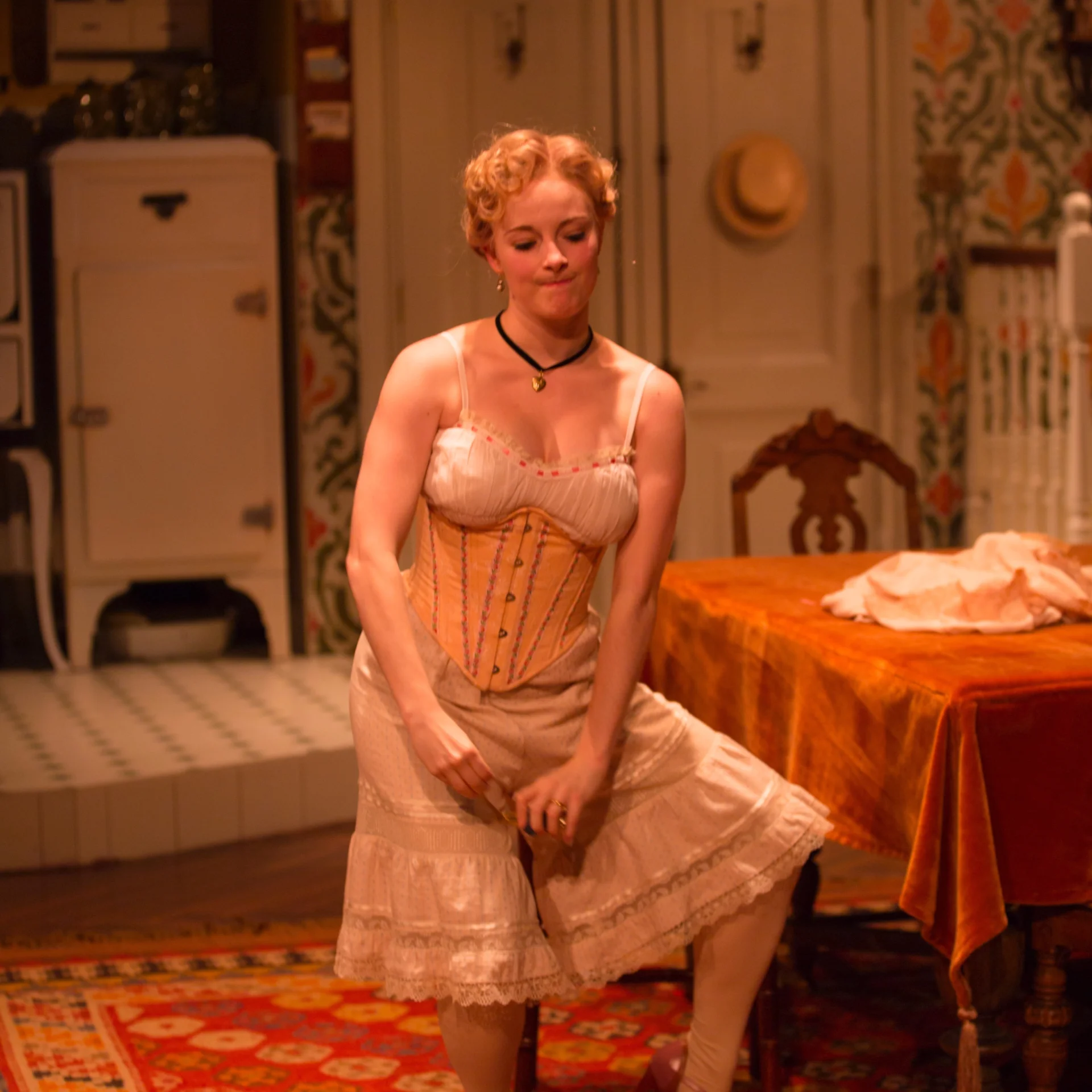 A woman in a corset awkwardly curtsies in a kitchen