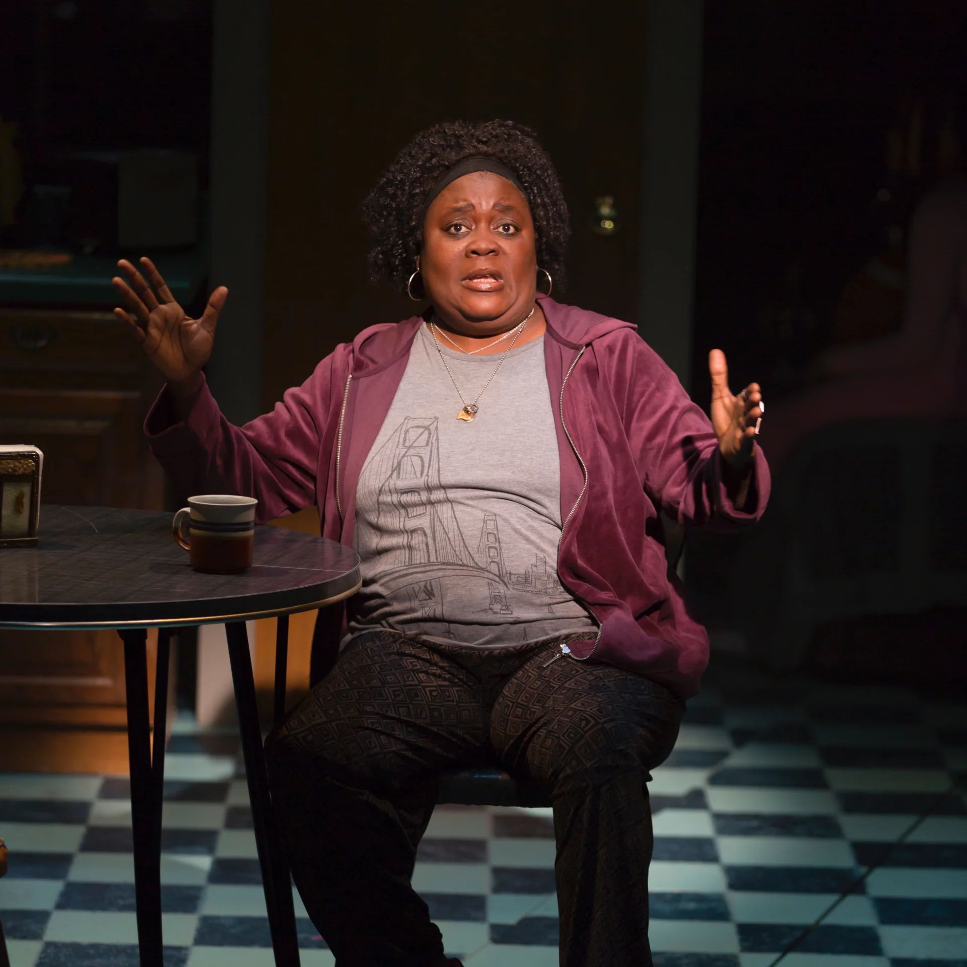 A women sitting at a kitchen table talks out to the audience