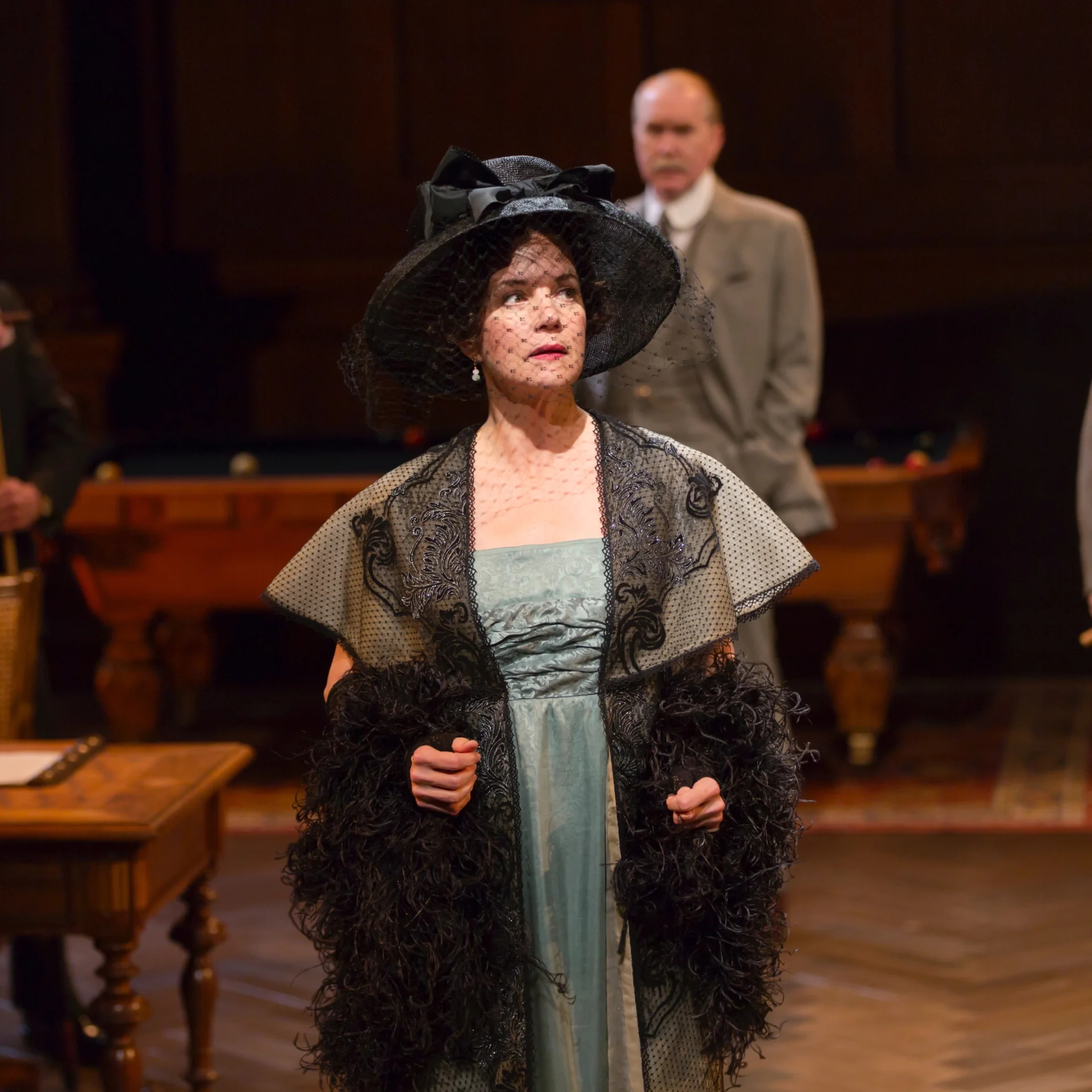 A woman in a fancy hat with net over her face looks out to her left