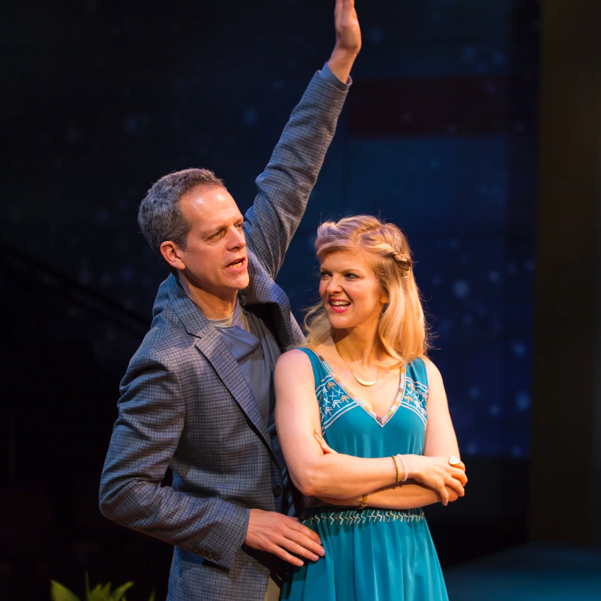 A man in a suit raises his arm behind a girl in a blue dress