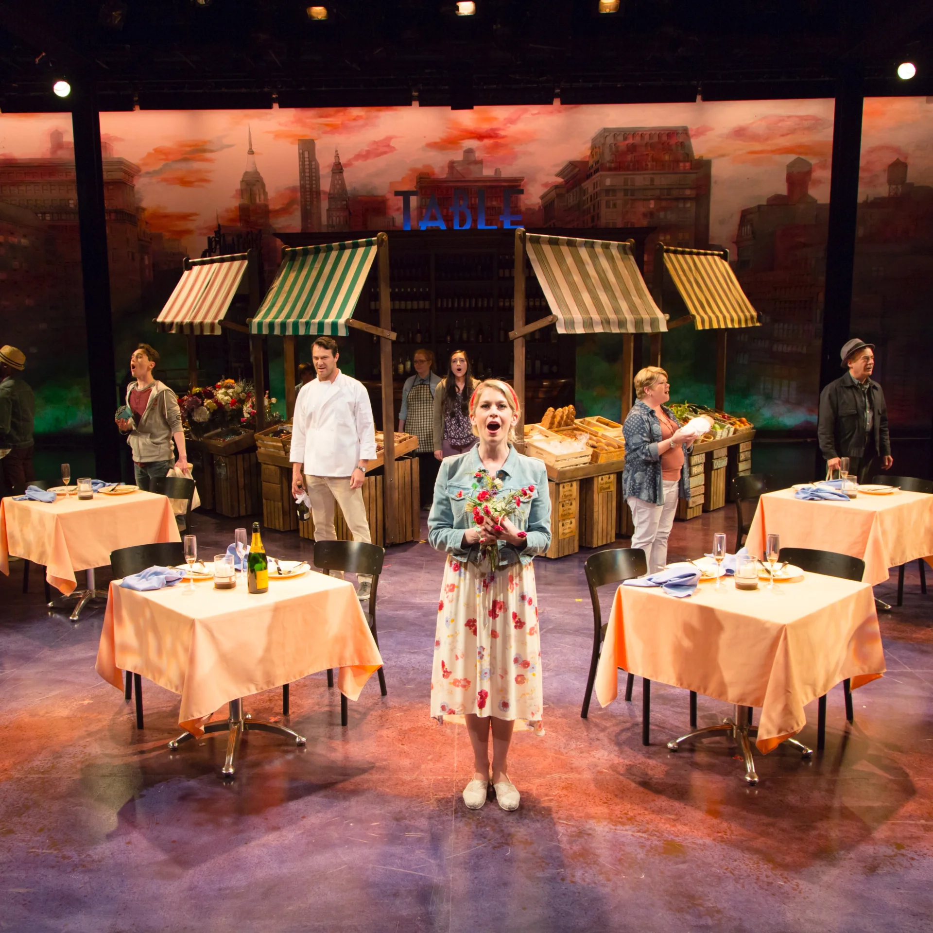 A woman holding flowers stands in the center of an outdoor marketplace