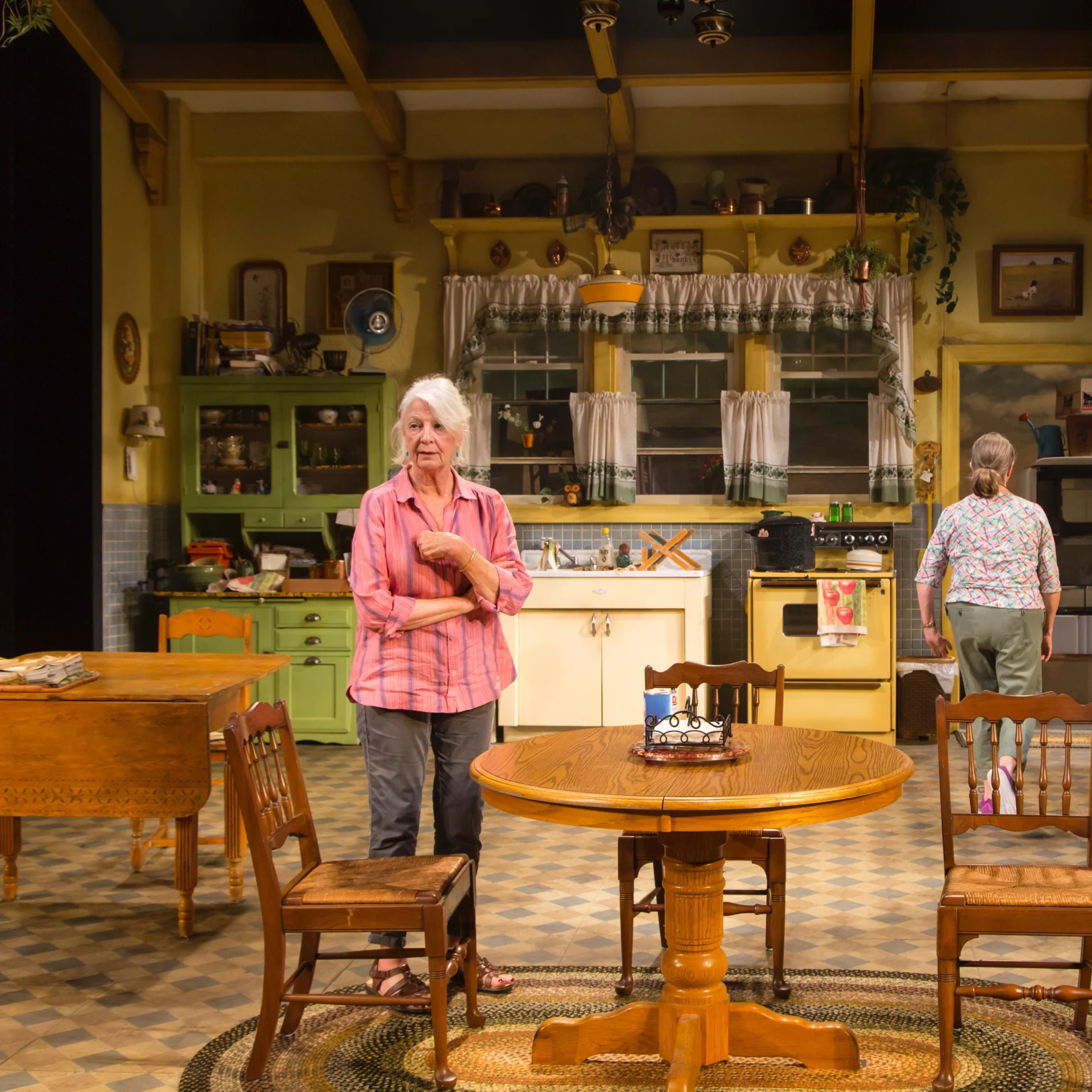 An older woman stands in a colorful kitchen