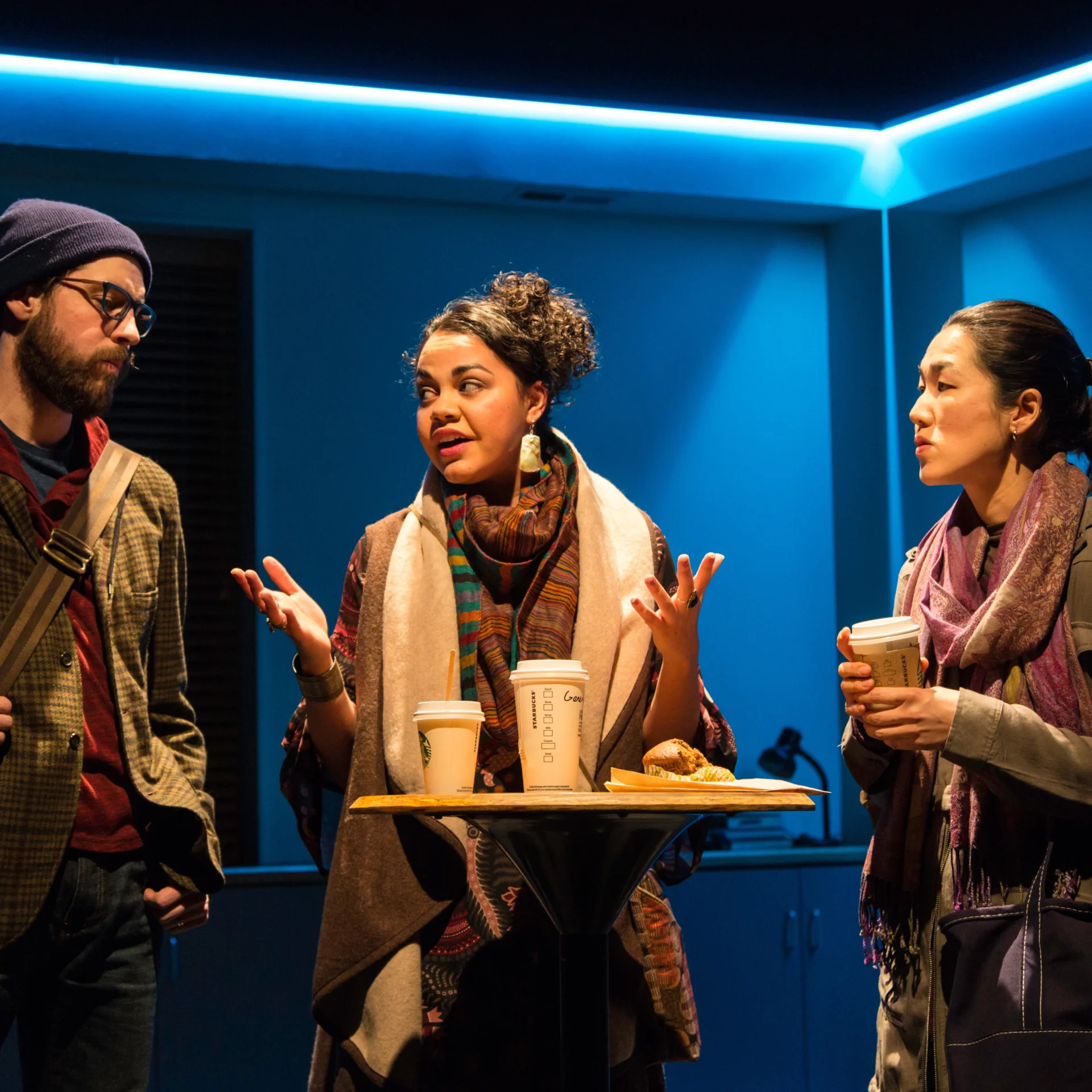 Three people with coffee talk around a standing table