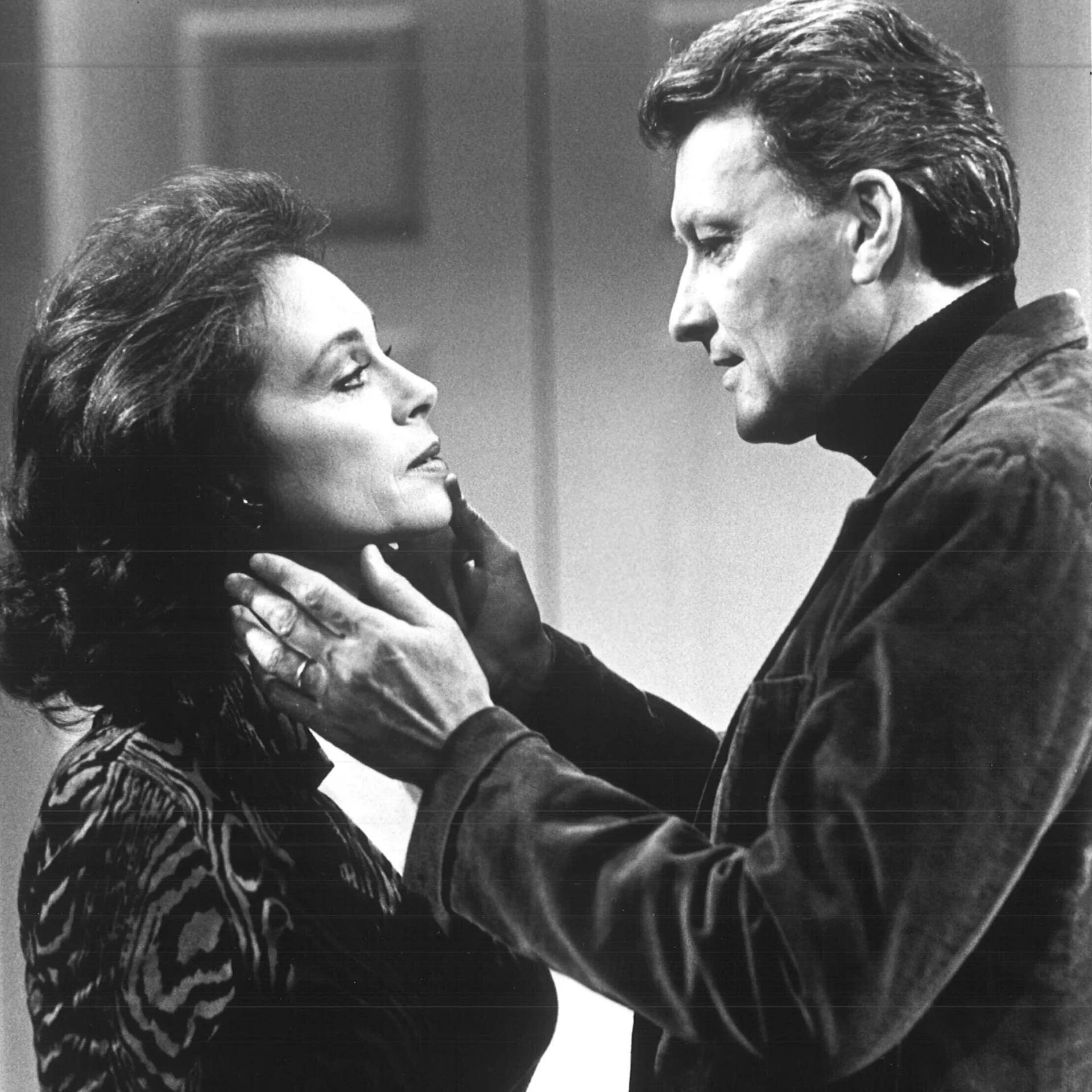 A woman and man are standing across from each other and the men is cupping the woman's cheeks.