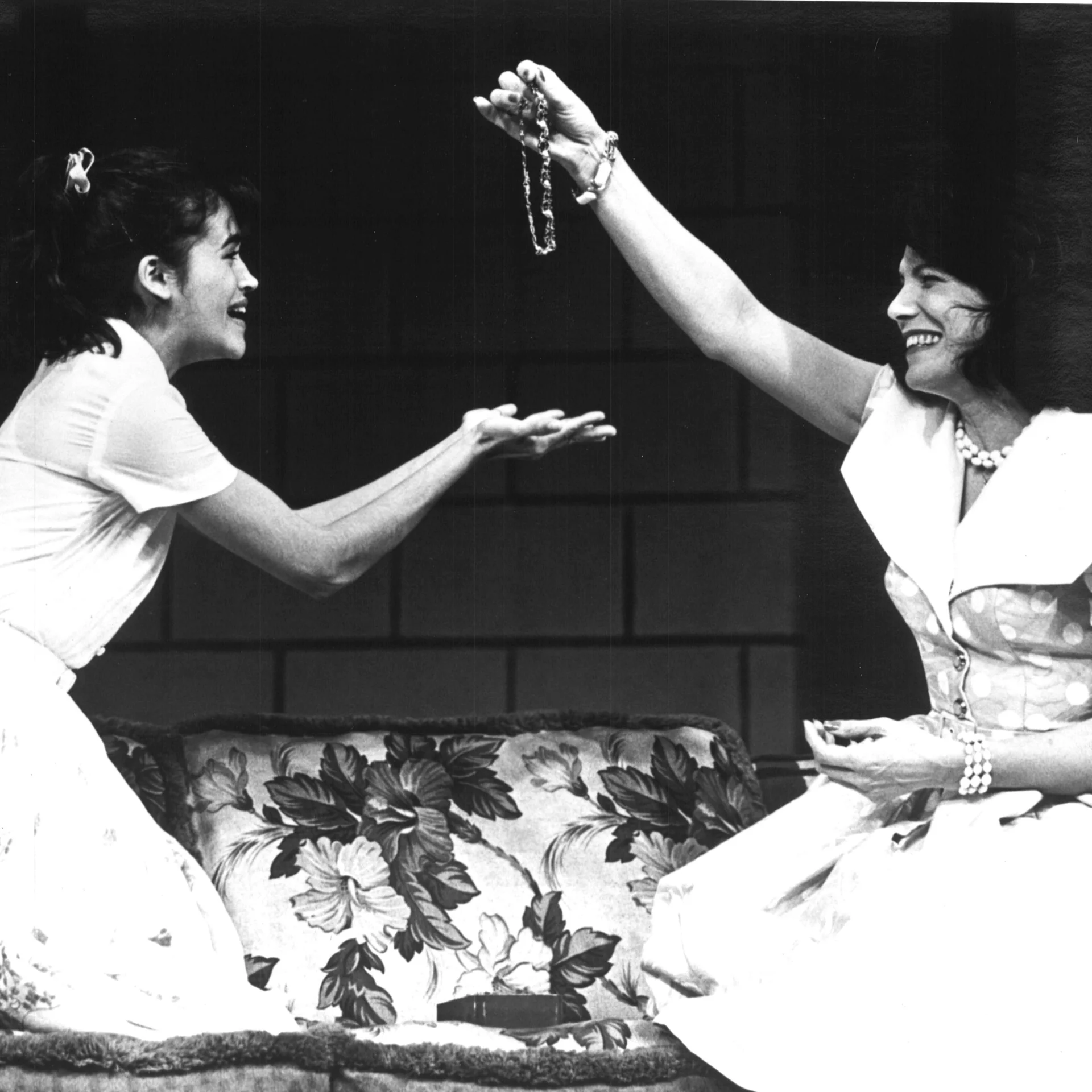 two woman are sitting together and one of them is handing the other one a necklace